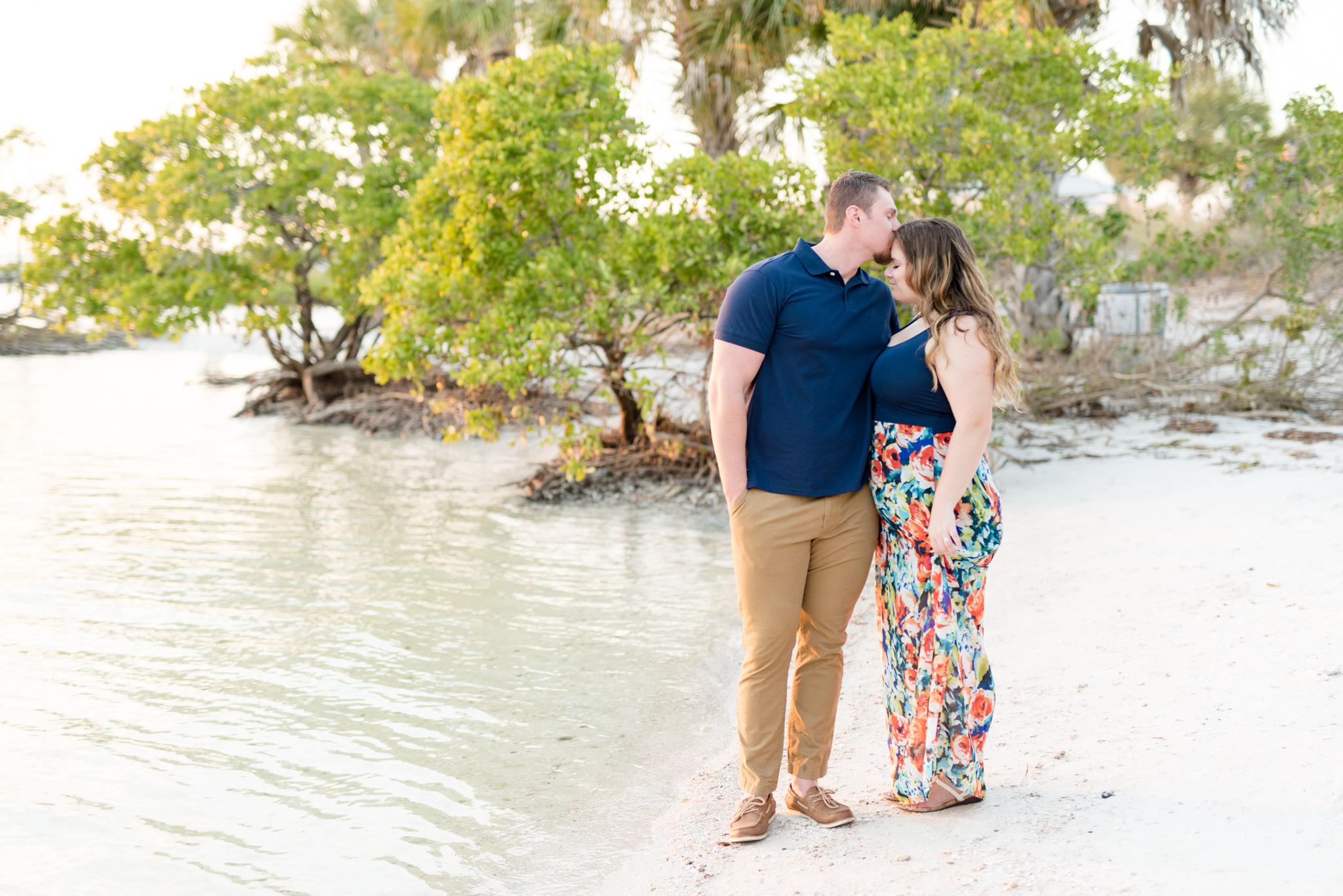 Groom kisses fiance's head on tropical beach.