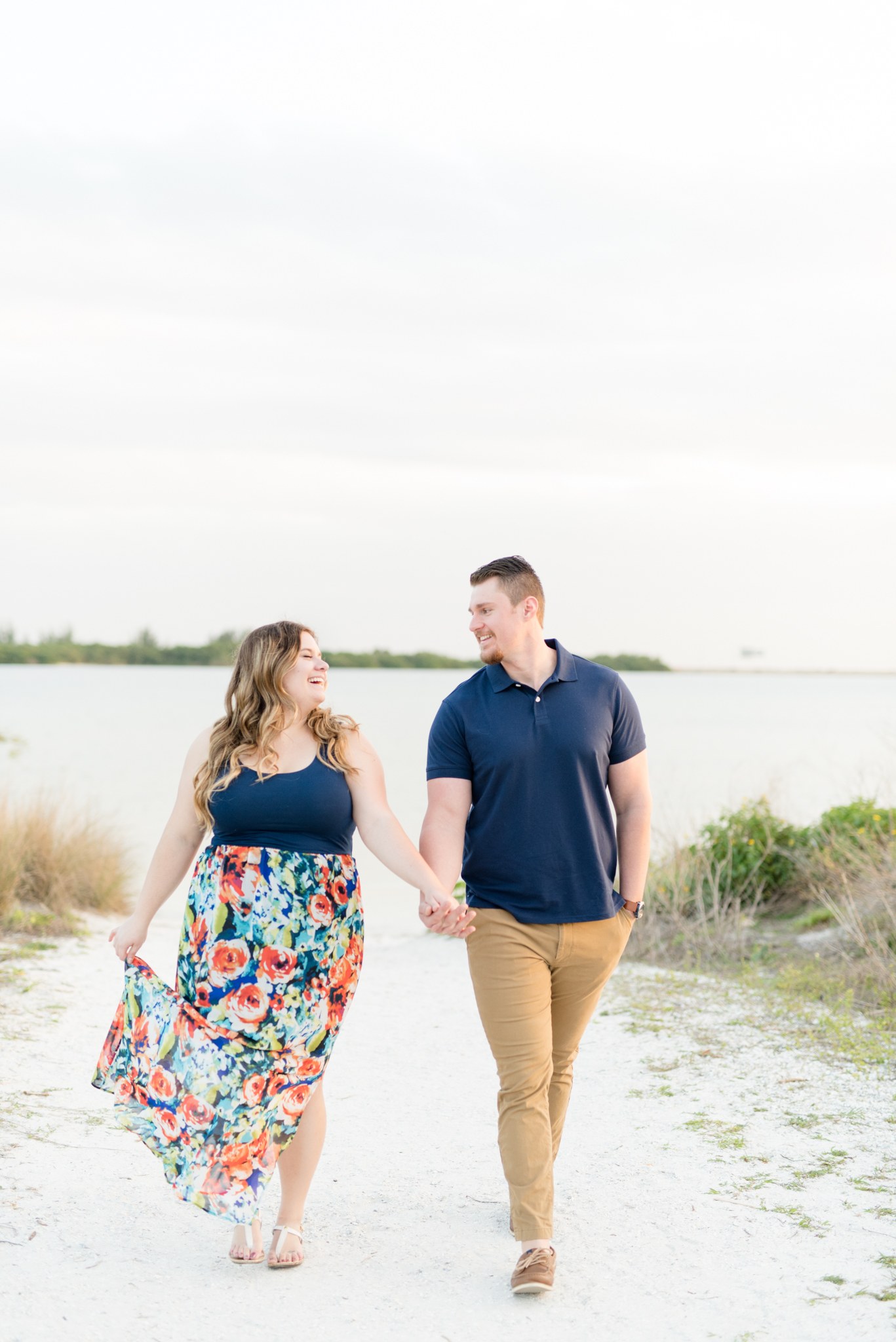 Couple laughs and walks on beach path.