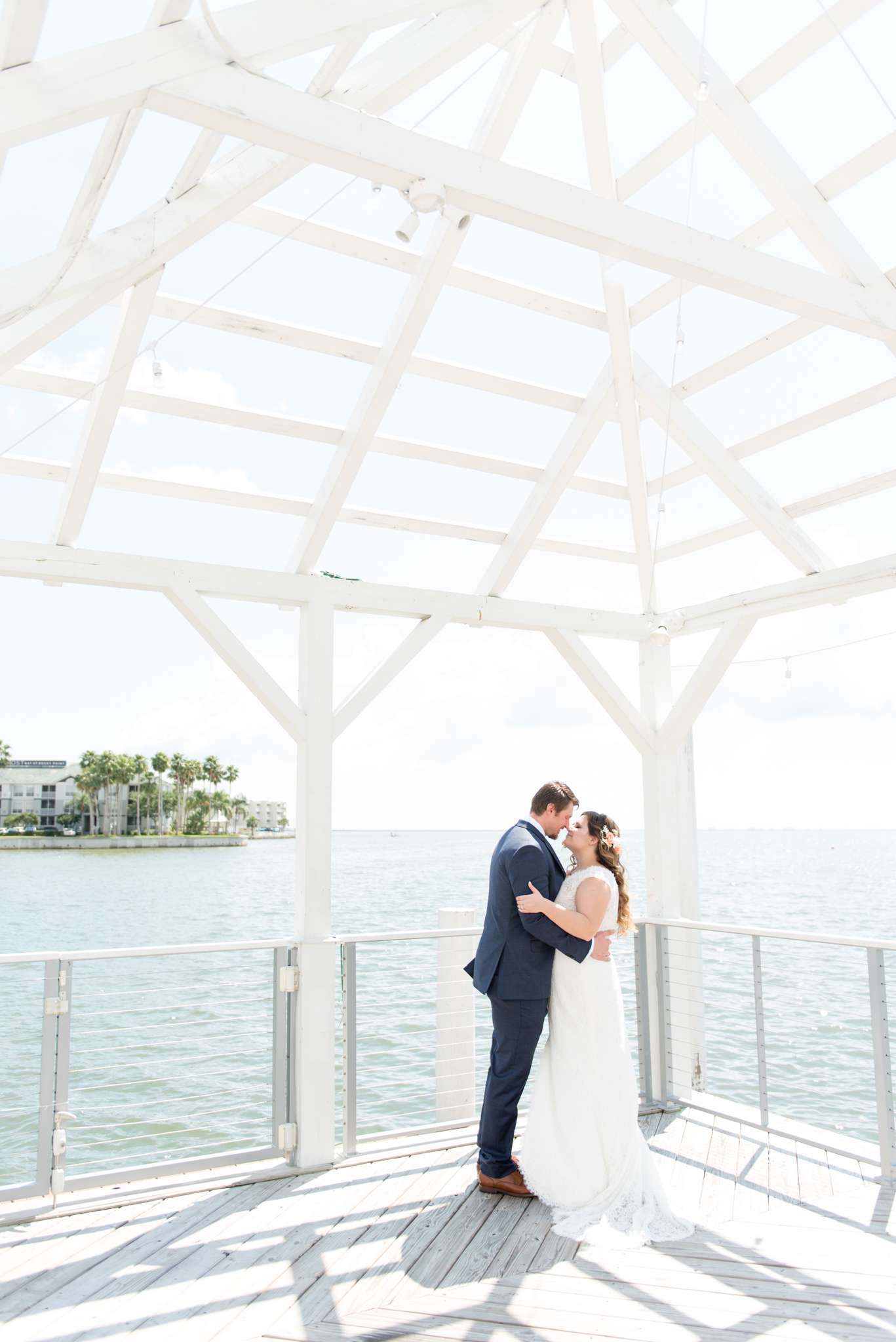 Bride and groom lean in for kiss on pier.