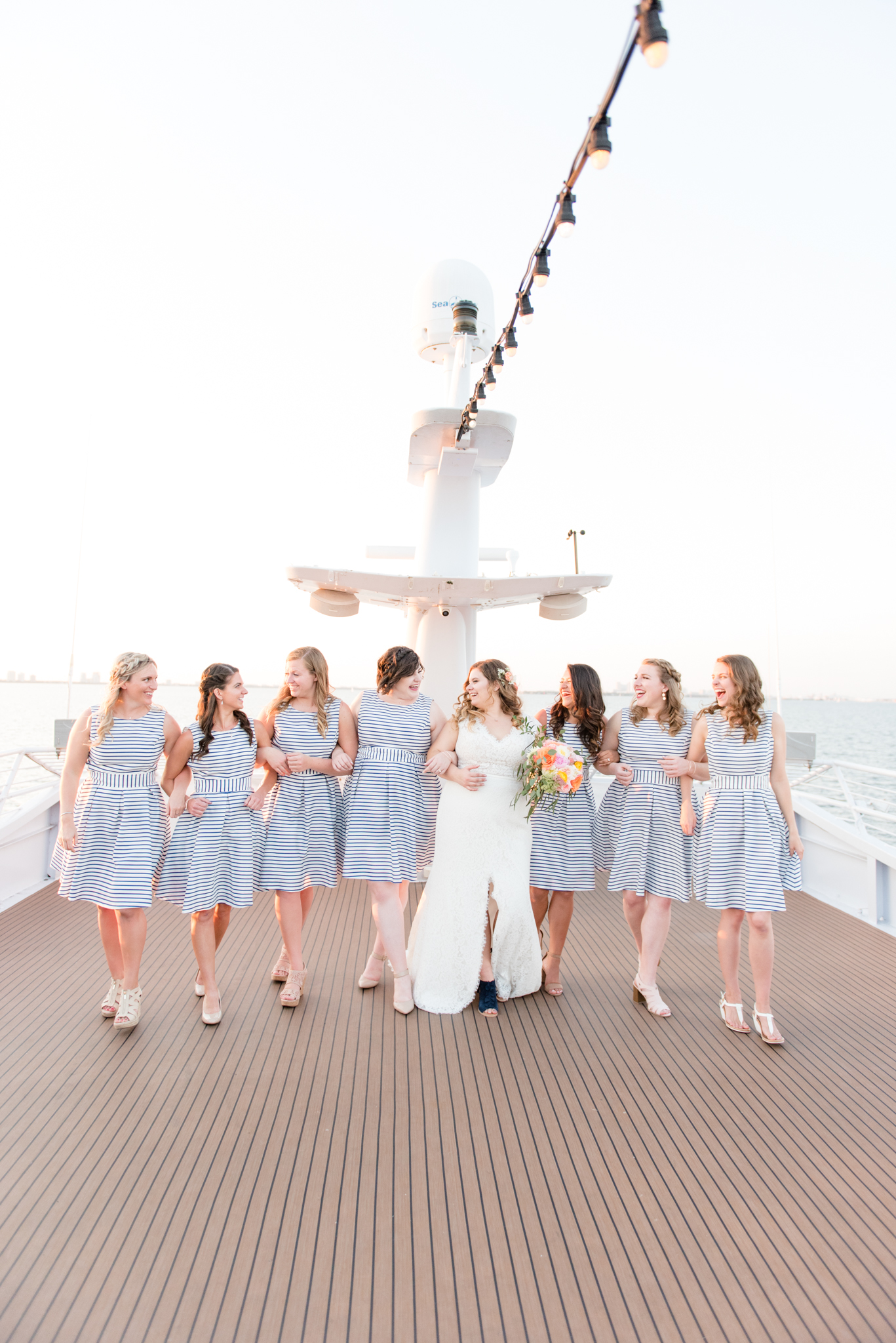 Bride and bridesmaids walk along yacht deck.