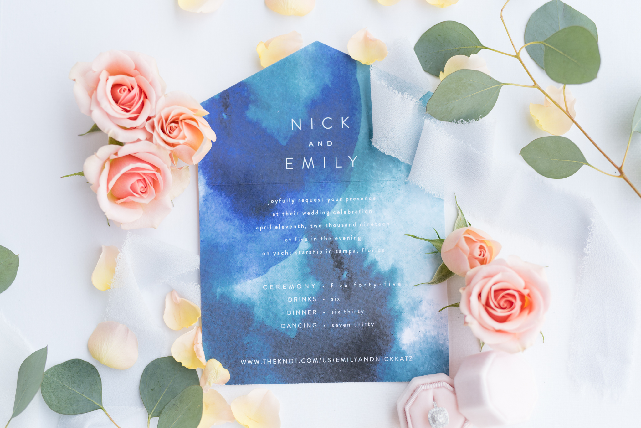 Wedding invitation sits with flower petals.