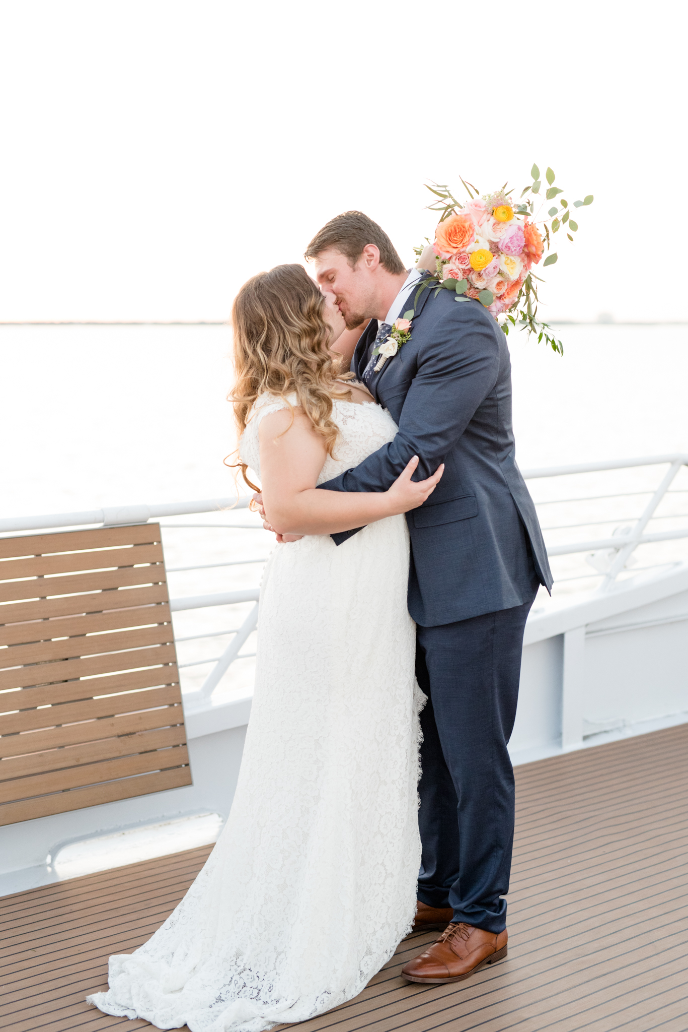 Bride and groom kiss on deck of yacht.