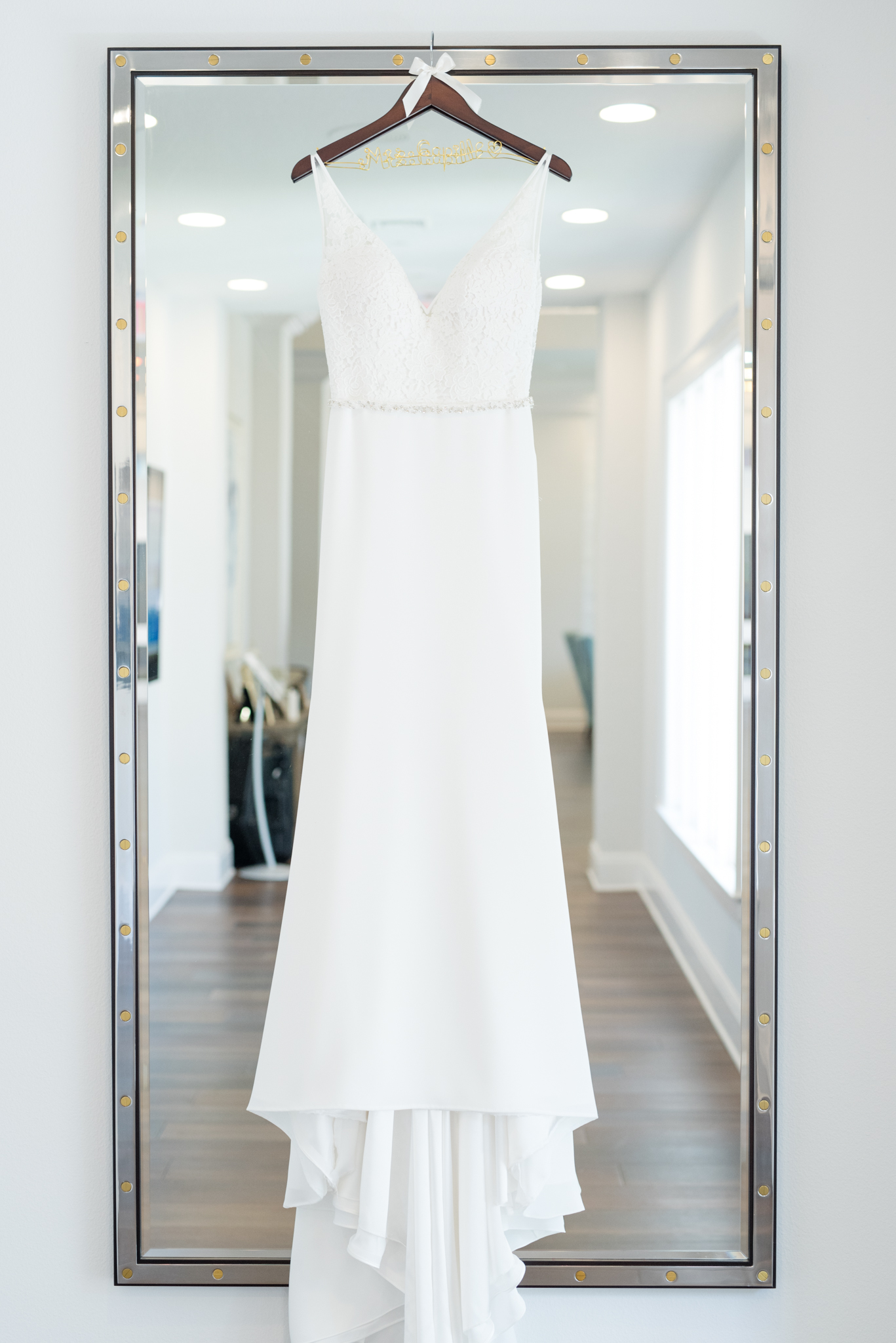 Wedding dress hangs on large mirror.