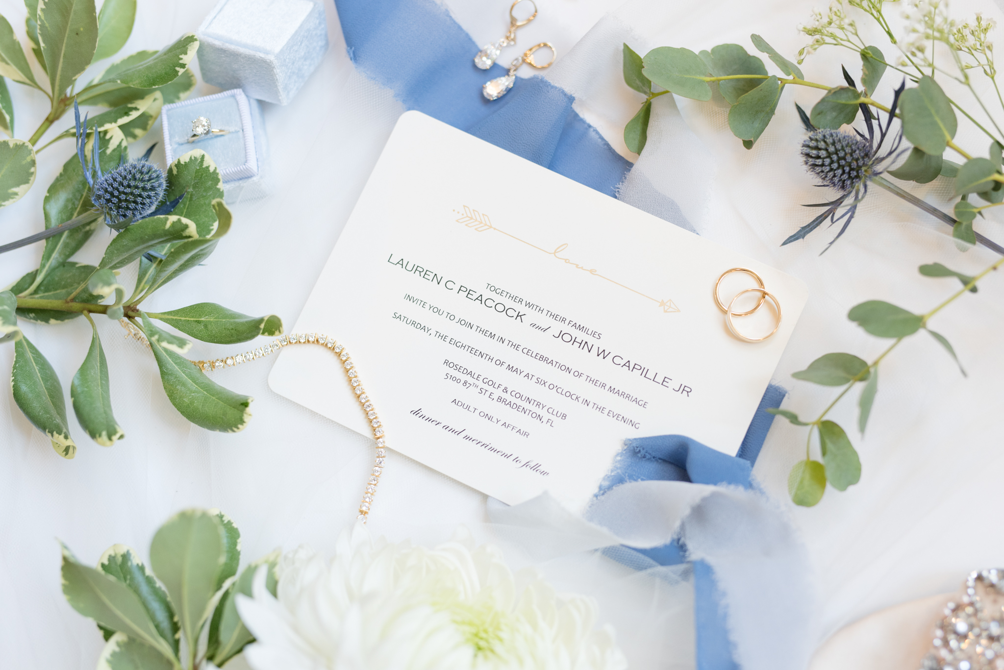 Wedding invitation sits with jewelry.