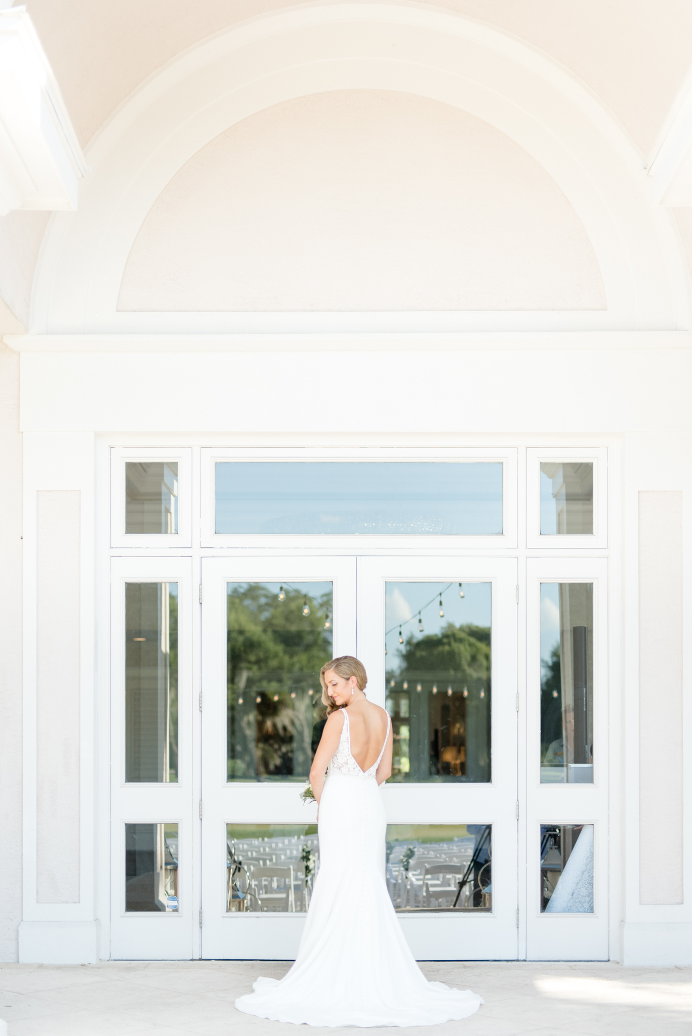 Bride stands in front of large windows.