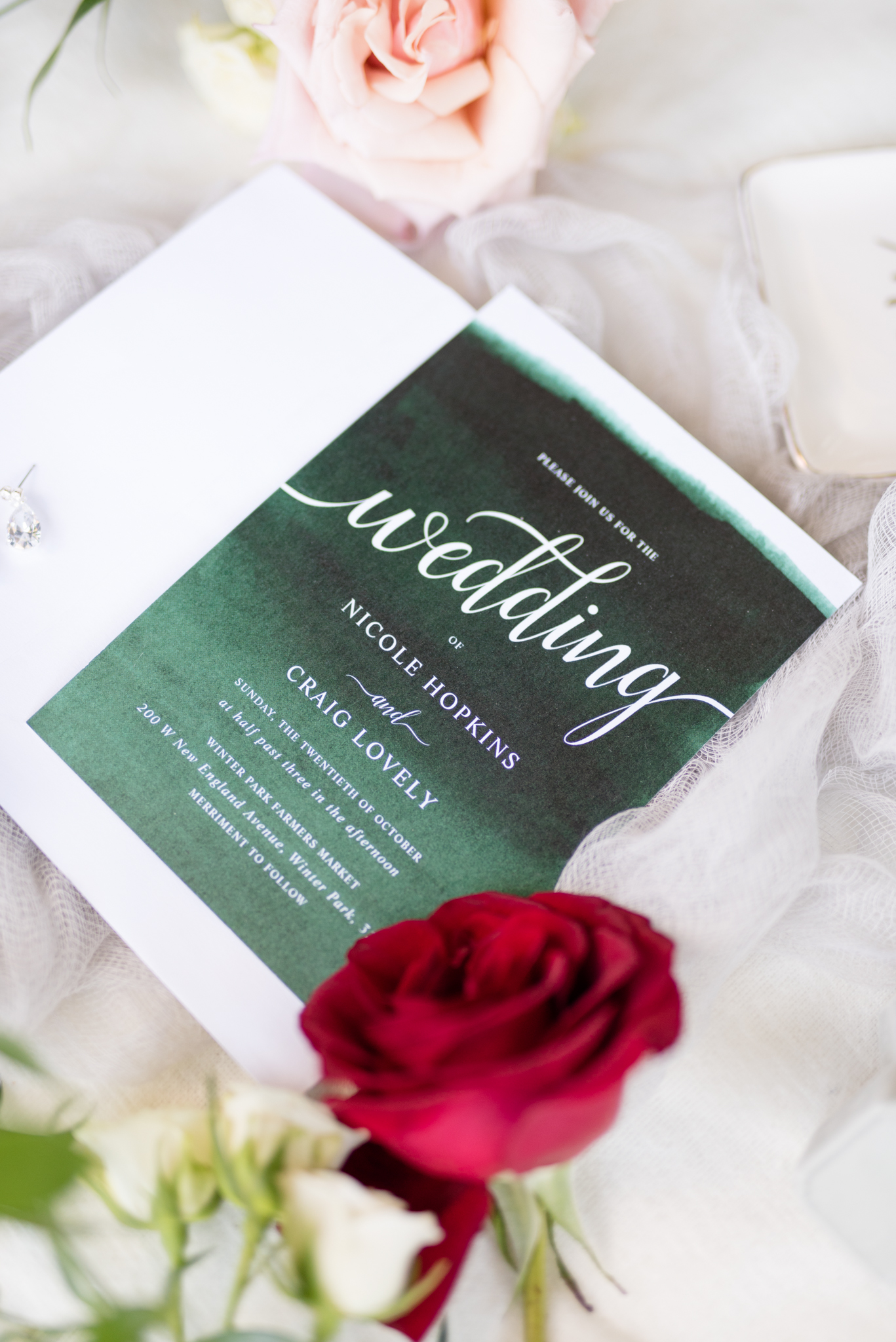Emerald wedding invitation sits with roses.