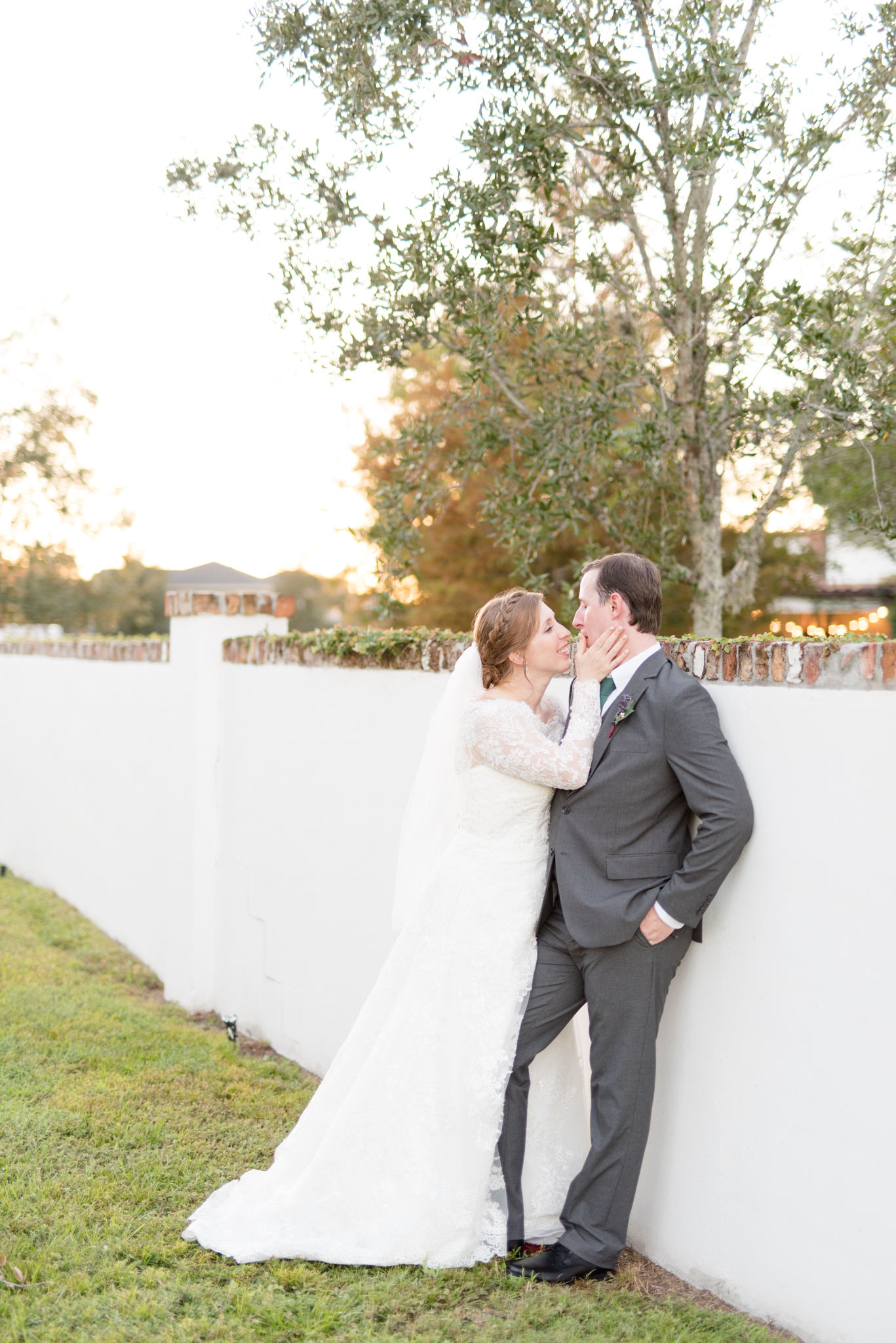 Bride and groom lean up against white brick wall.