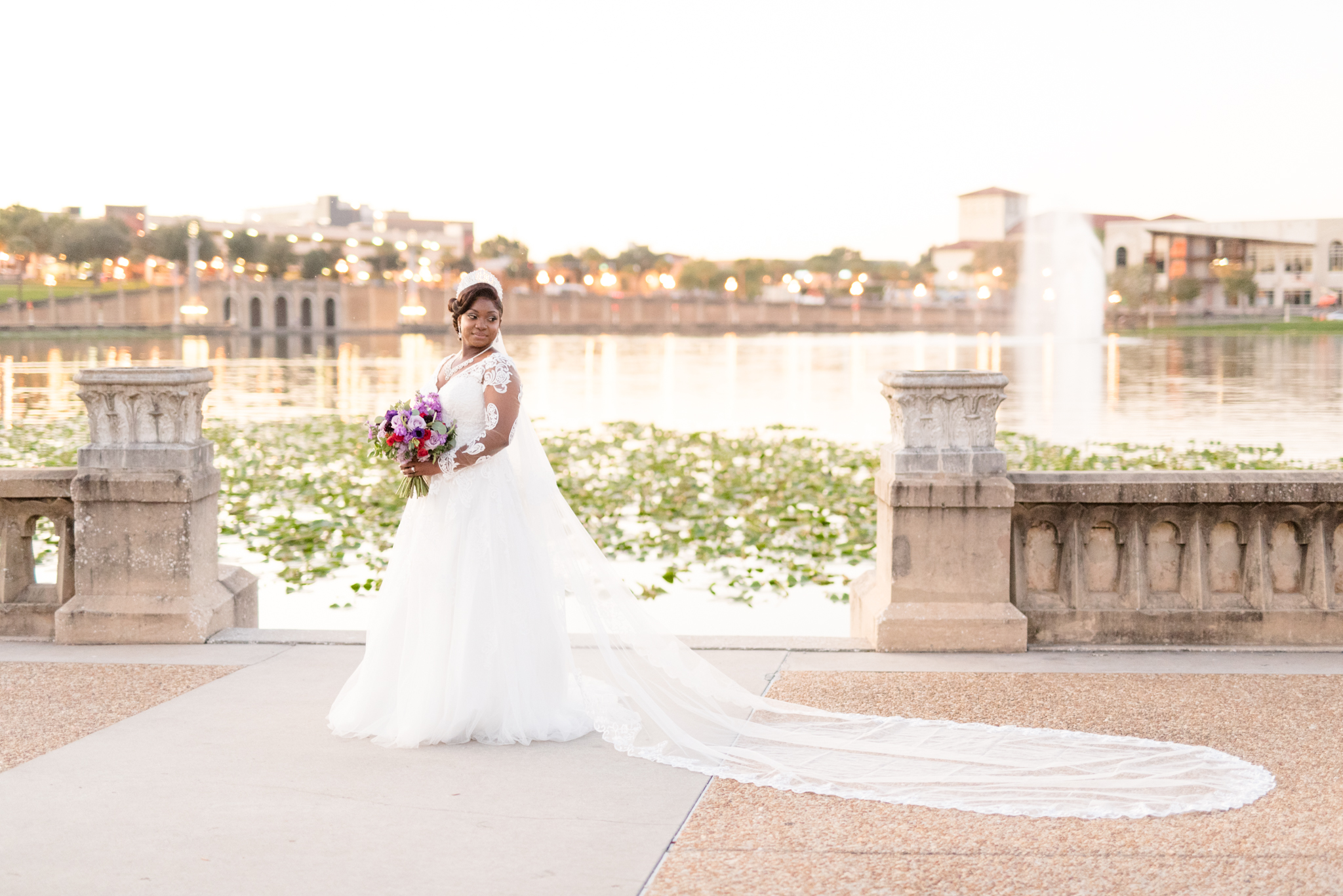 Bride looks over shoulder by lake at sunset.