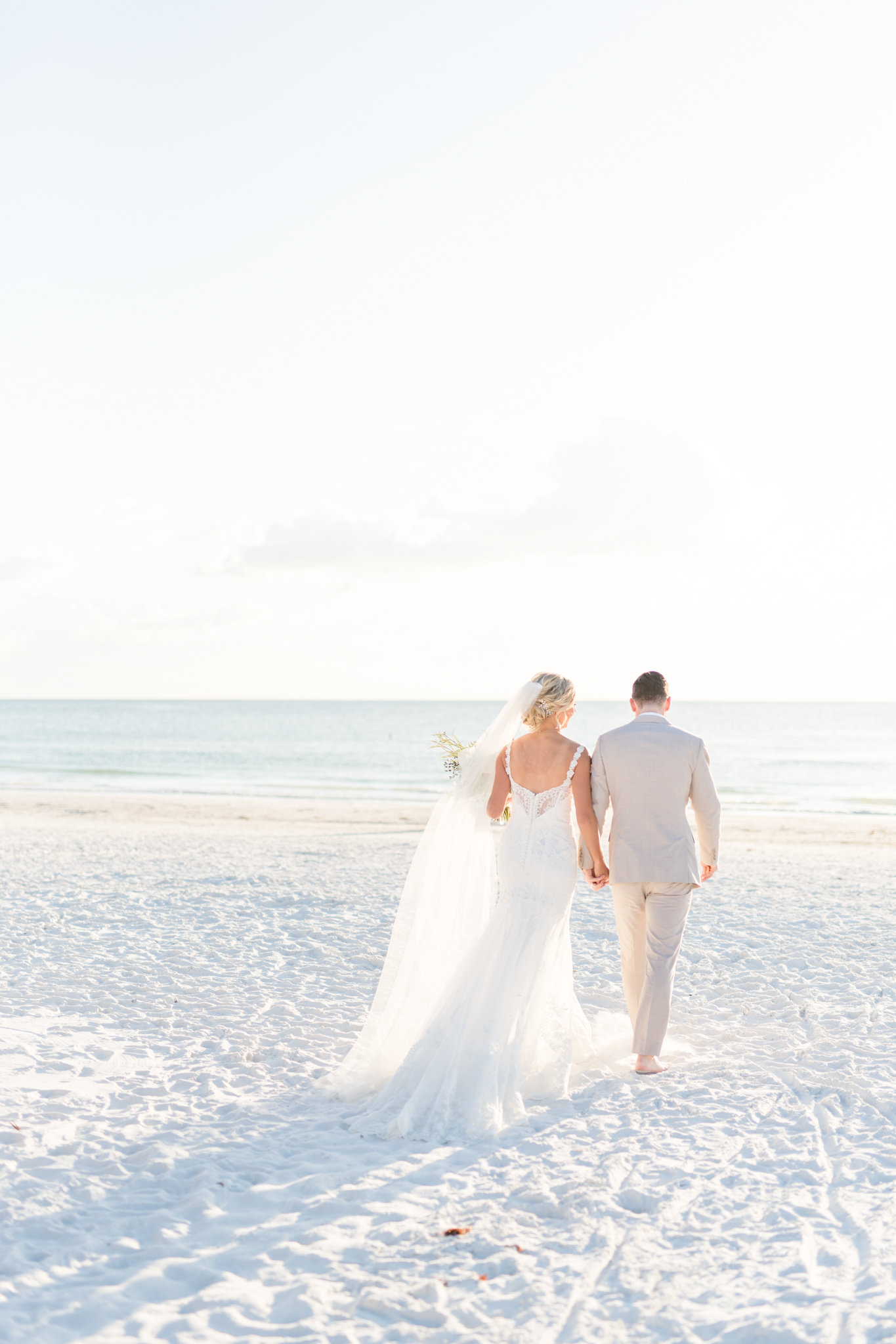 Bride and groom walk along beach.