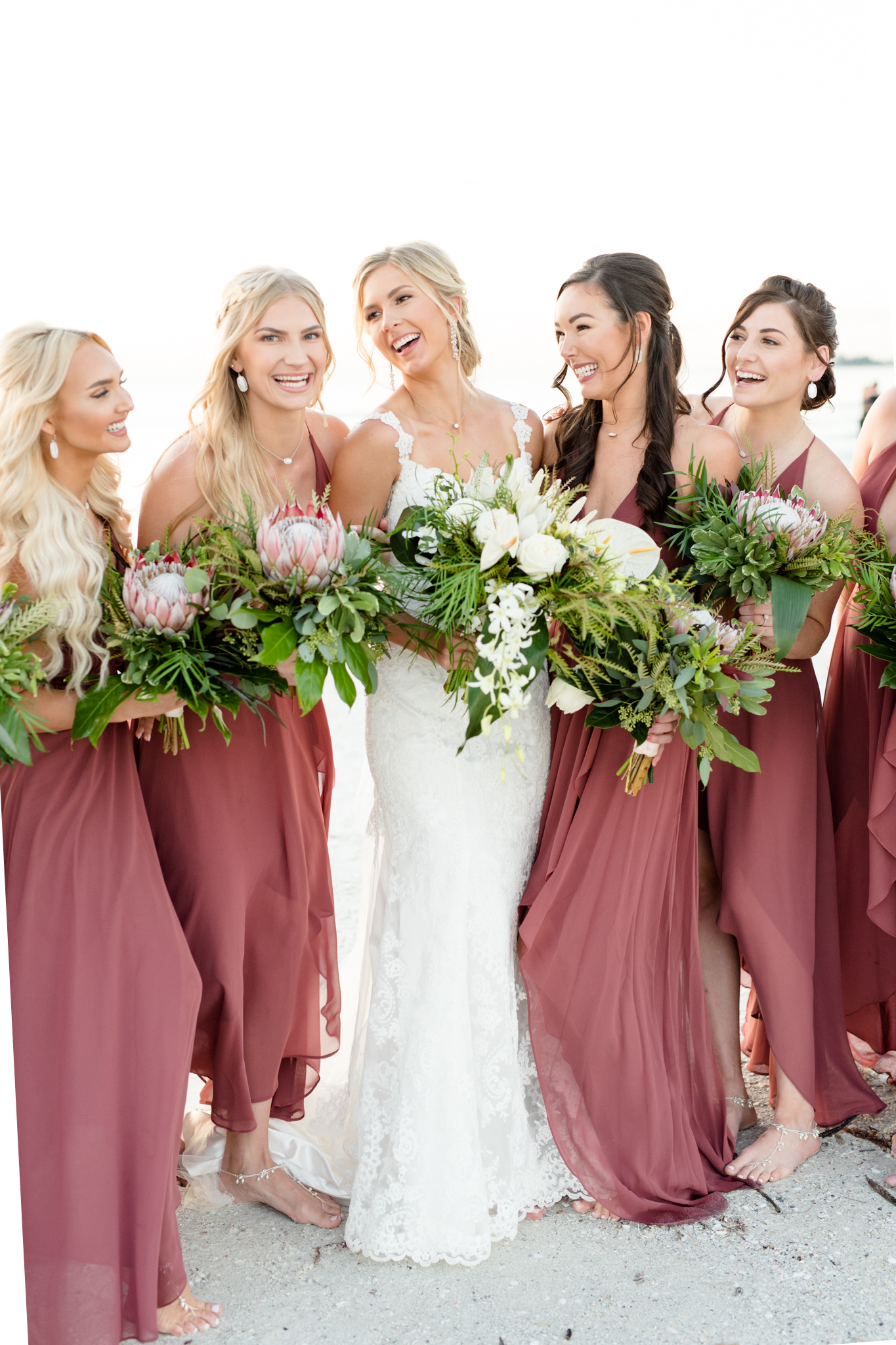 Bride and bridesmaids laugh together at sunset.