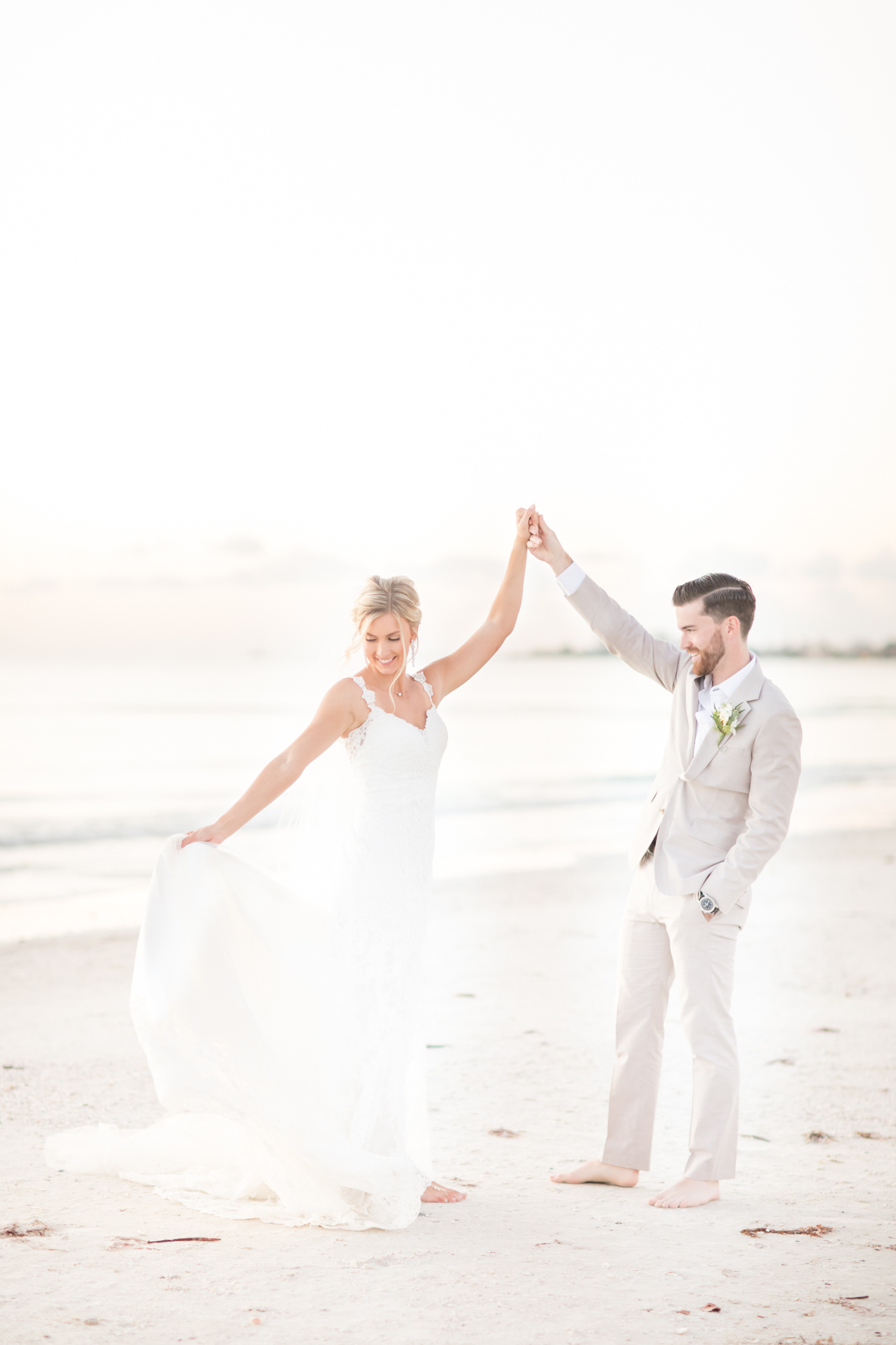 Groom twirls bride on beach.