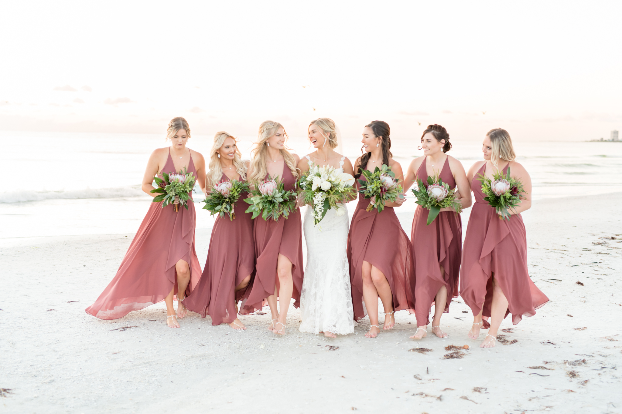 Bride and bridesmaids walk together on sunset beach.