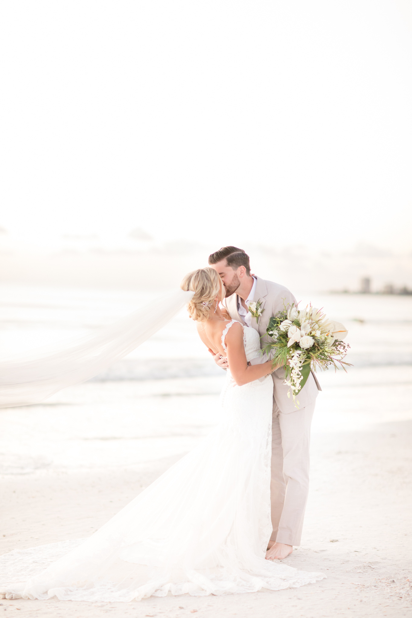 Bride and groom embrace and kiss at sunset.