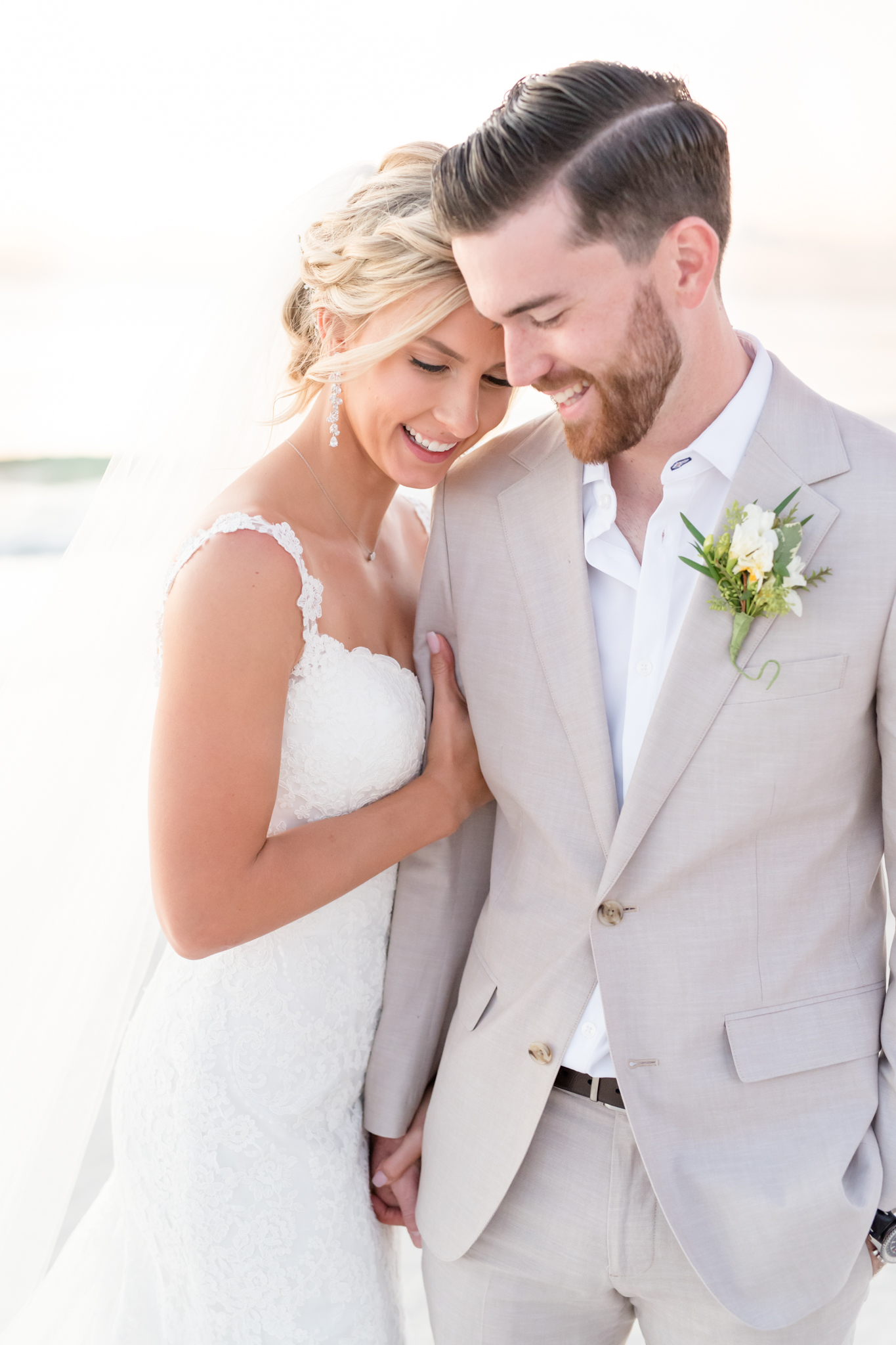 Bride and groom embrace on beach at sunset.