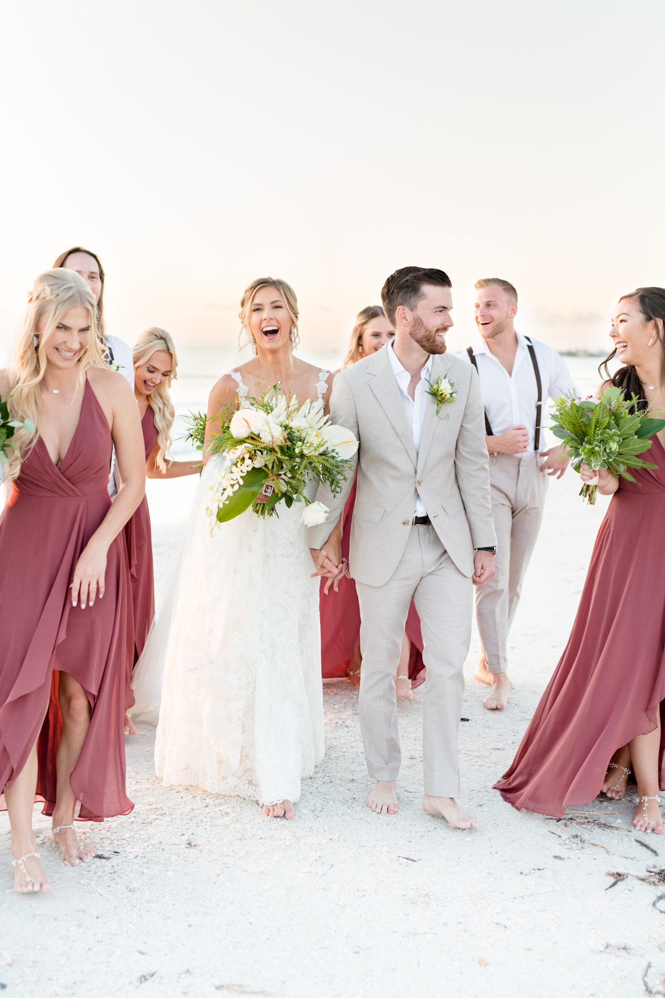 Wedding party laughs as they walk across the beach.