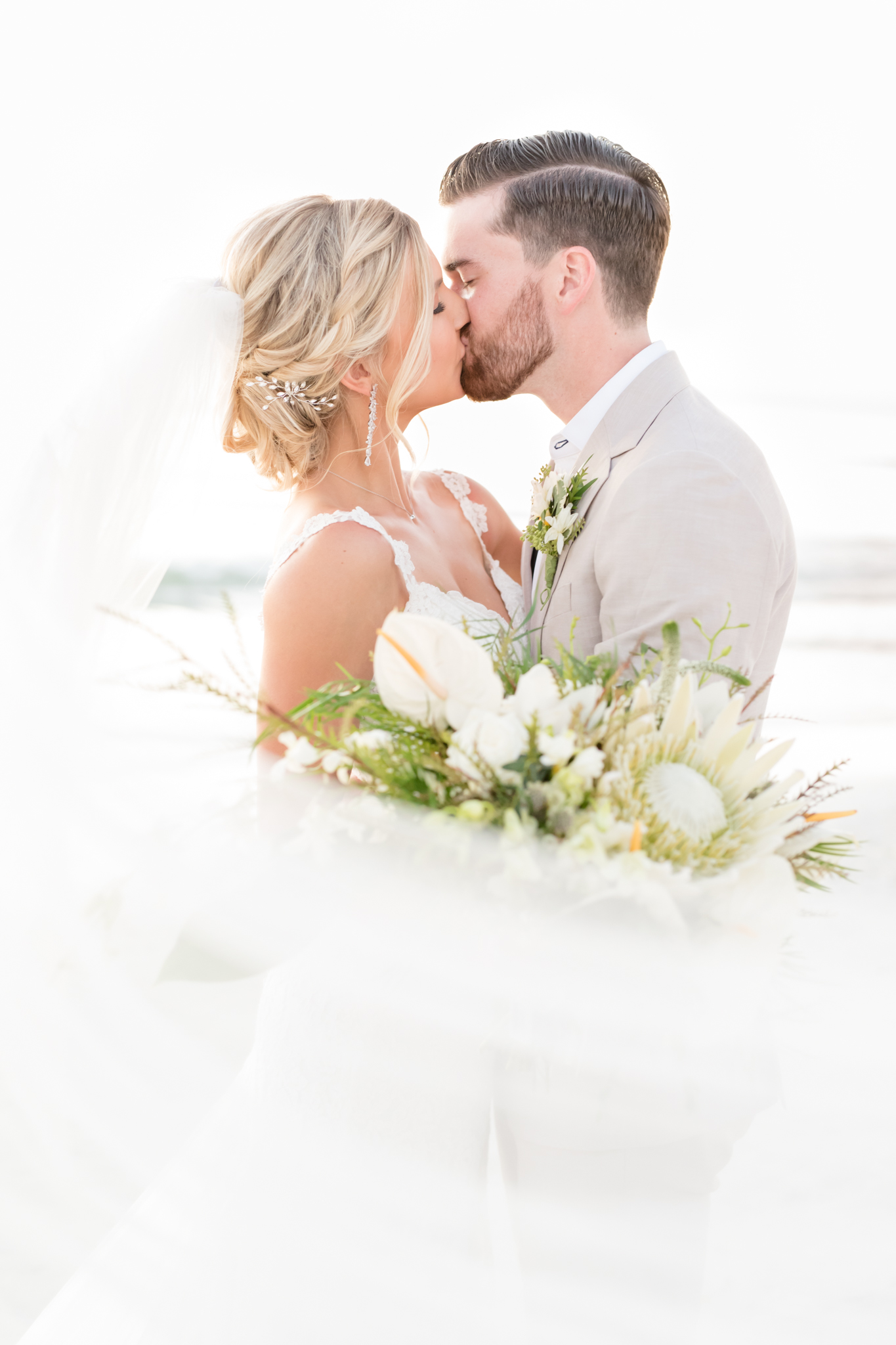 Bride and groom kiss while veil blows in wind.