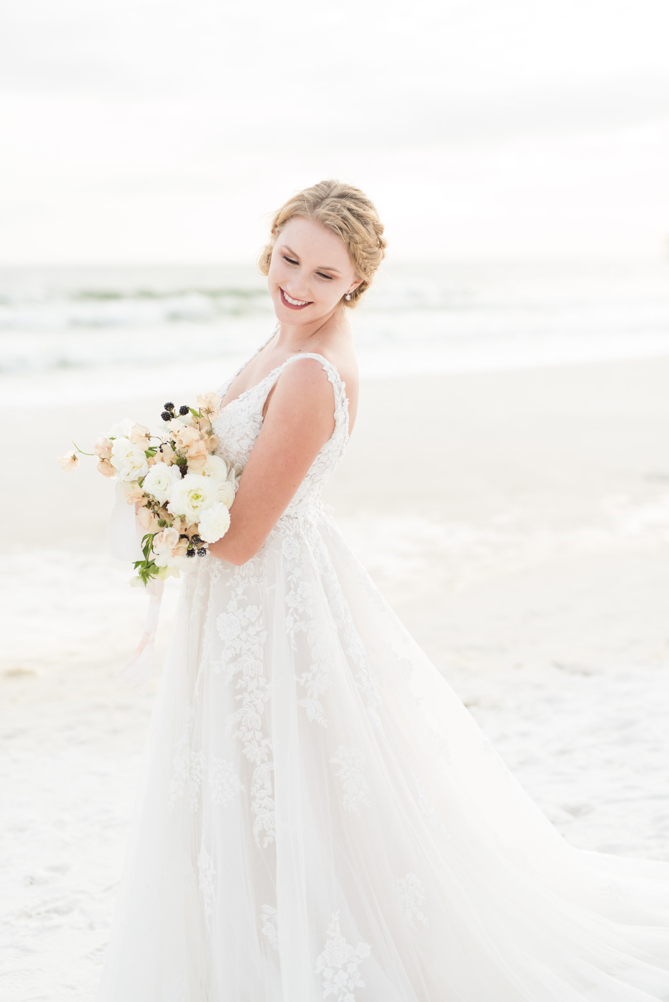 Bride smiles down shoulder on beach.
