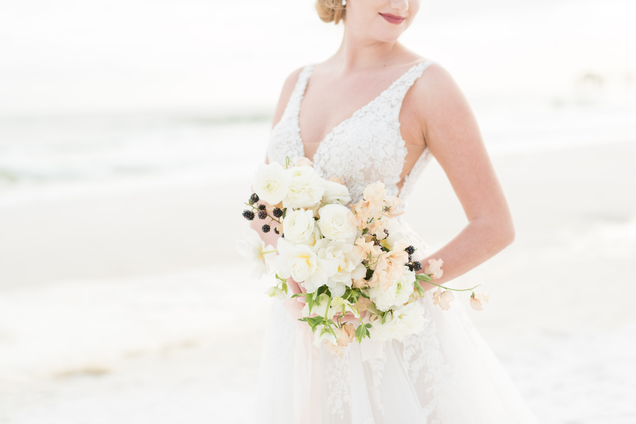 Bride holds bouquet by ocean at sunset.