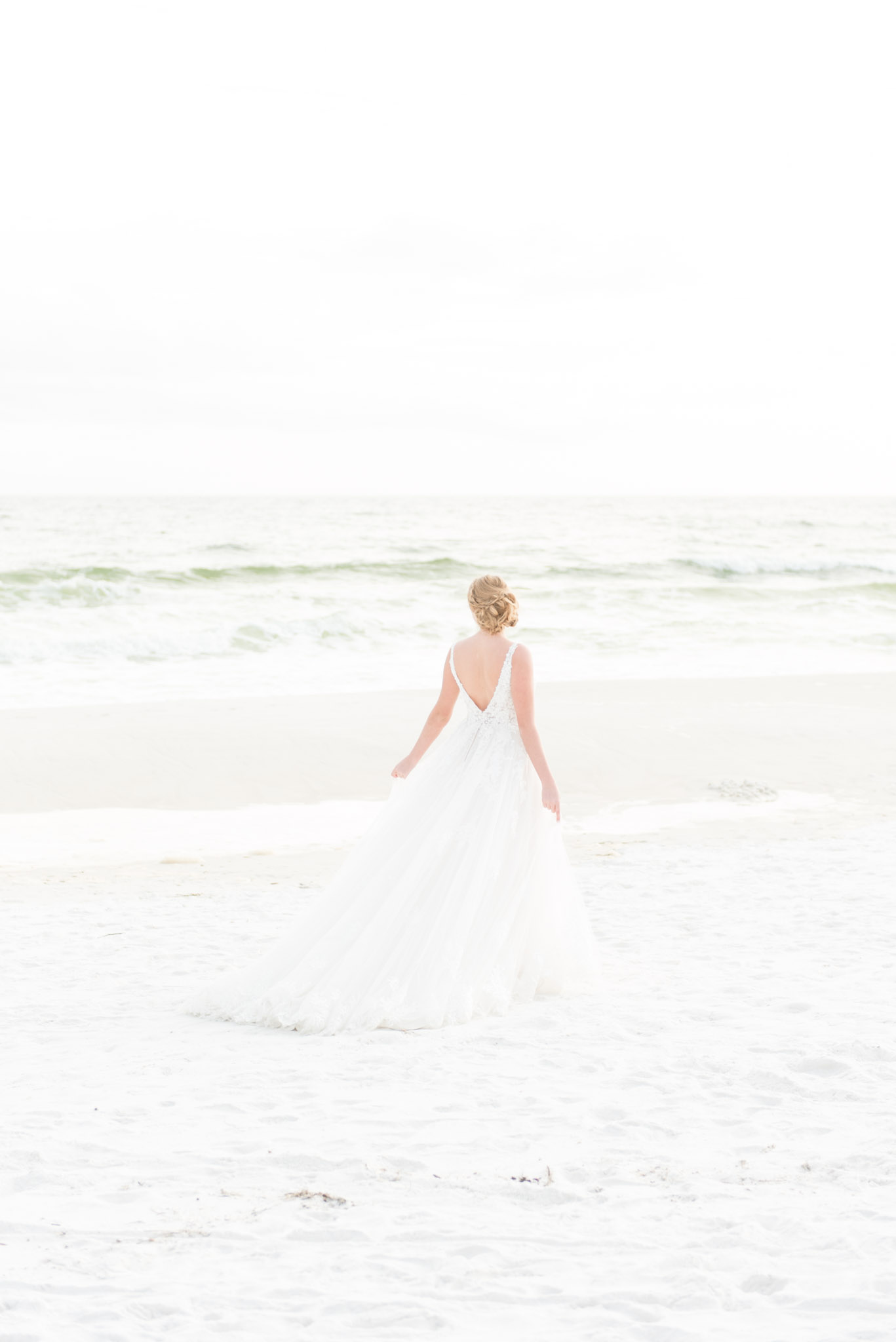 Bride walks by ocean at sunset.