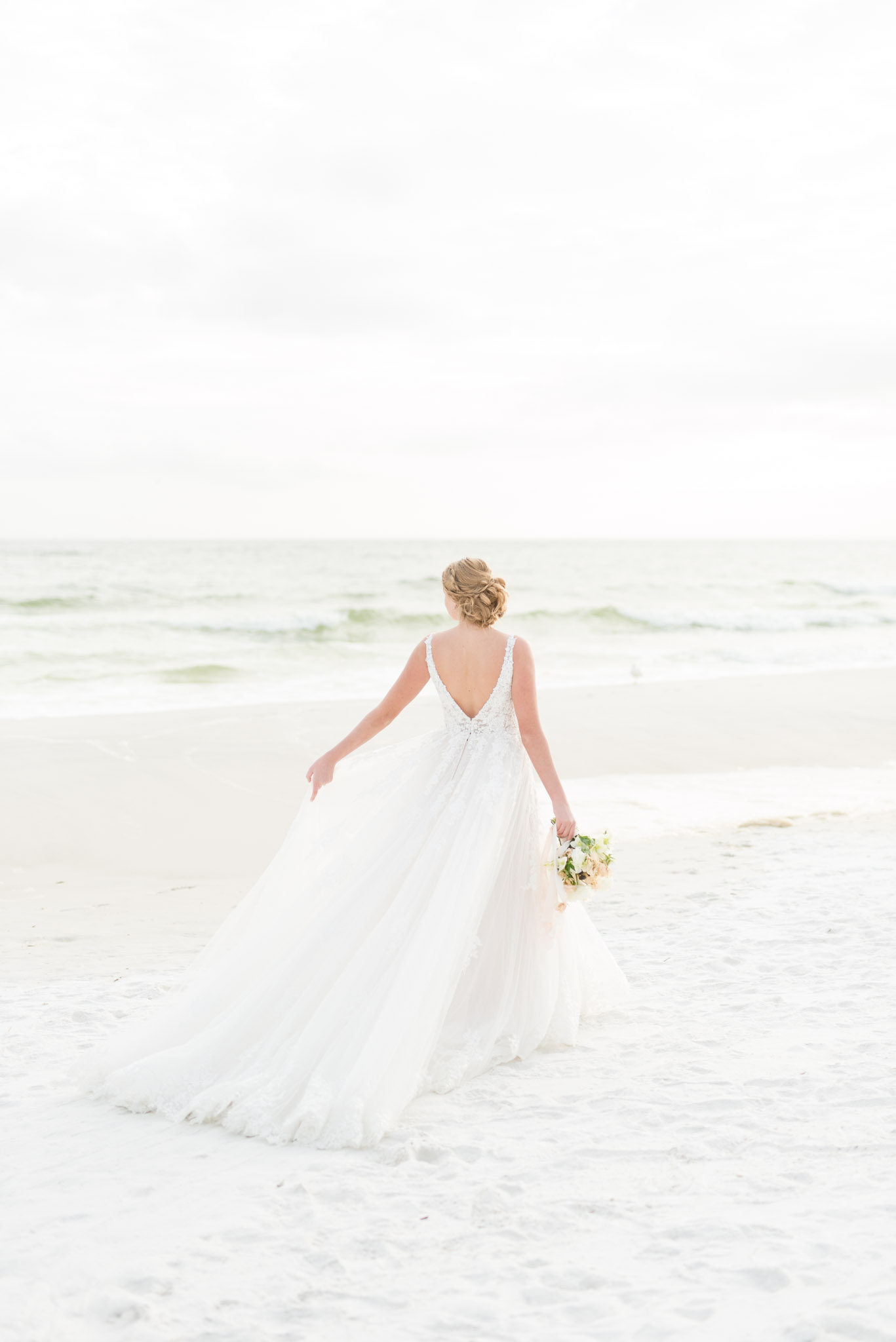 Bride swishes wedding gown on beach.
