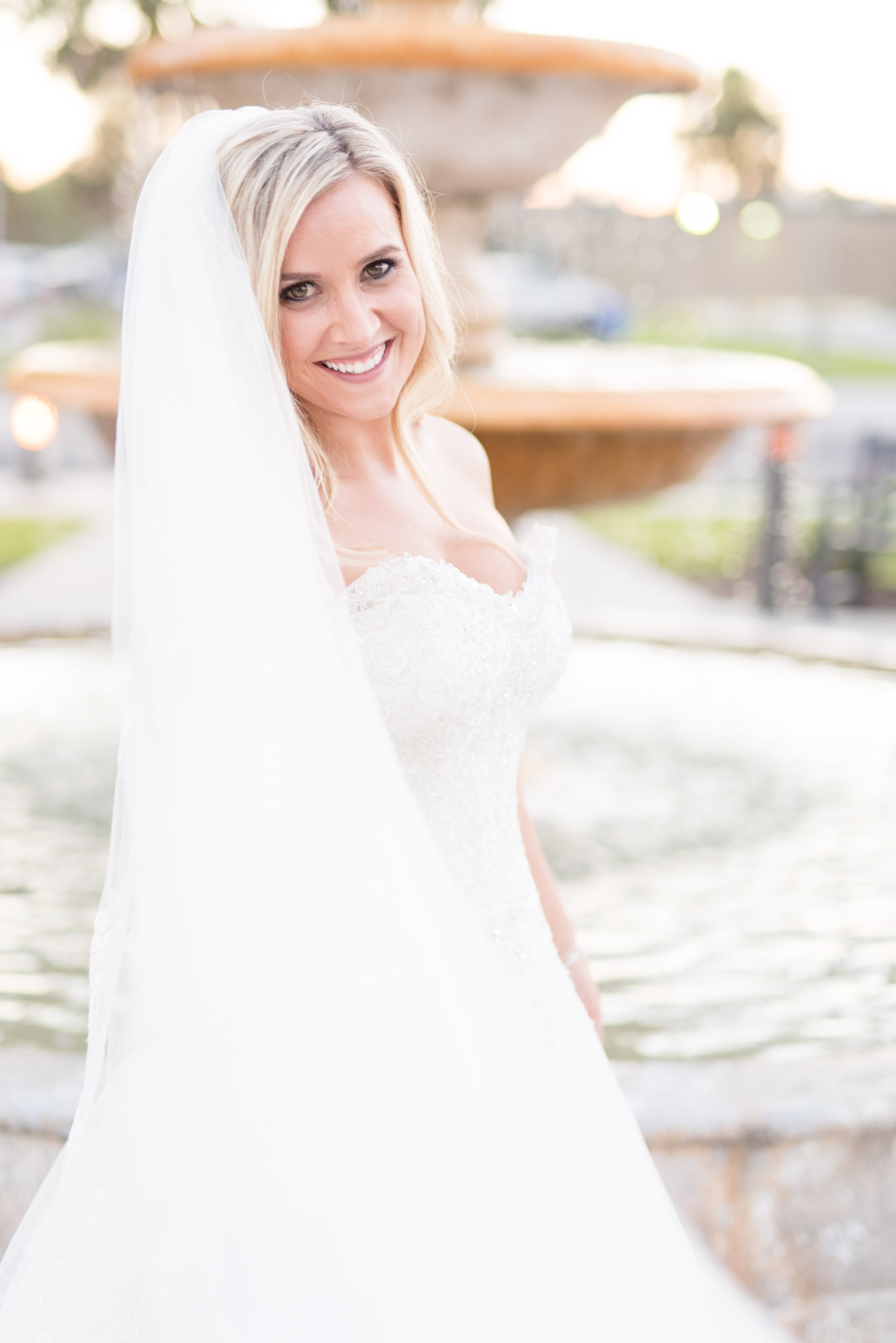 Bride smiles as veil blows in wind.