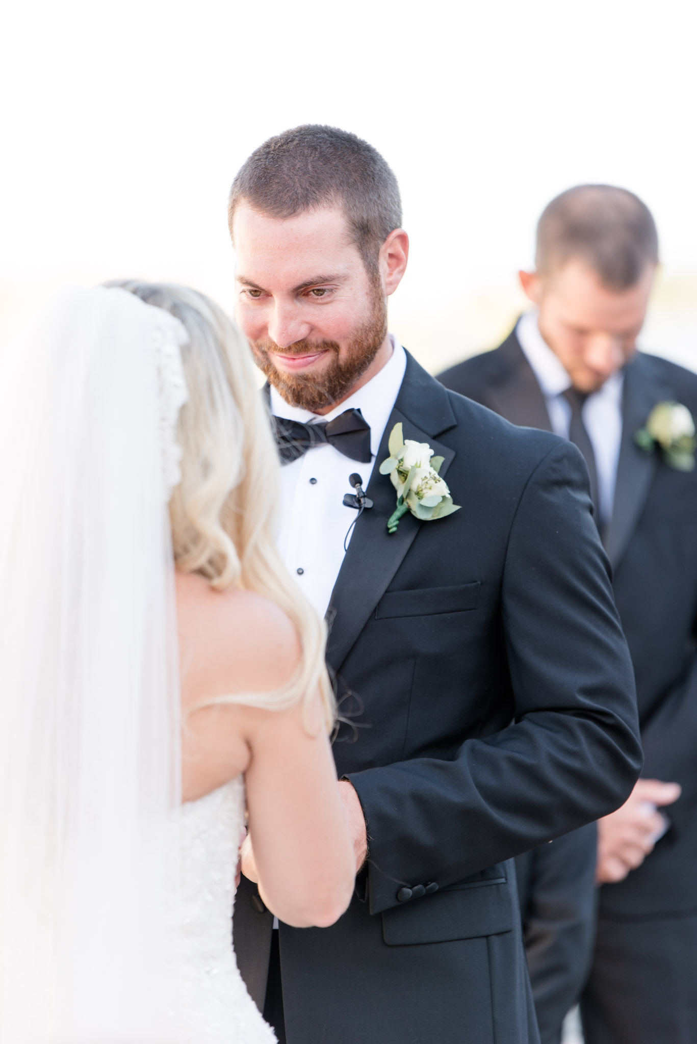 Groom smiles at bride during wedding ceremony.
