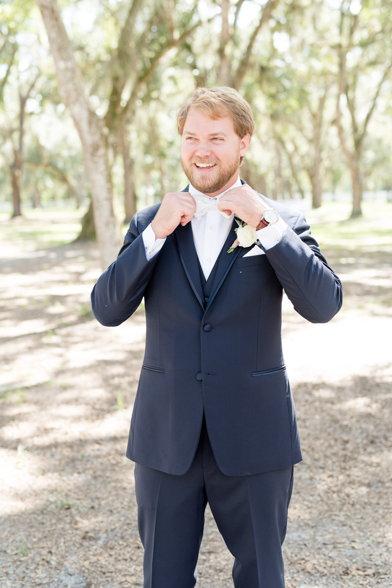 Groom smiles and straightens bow tie.