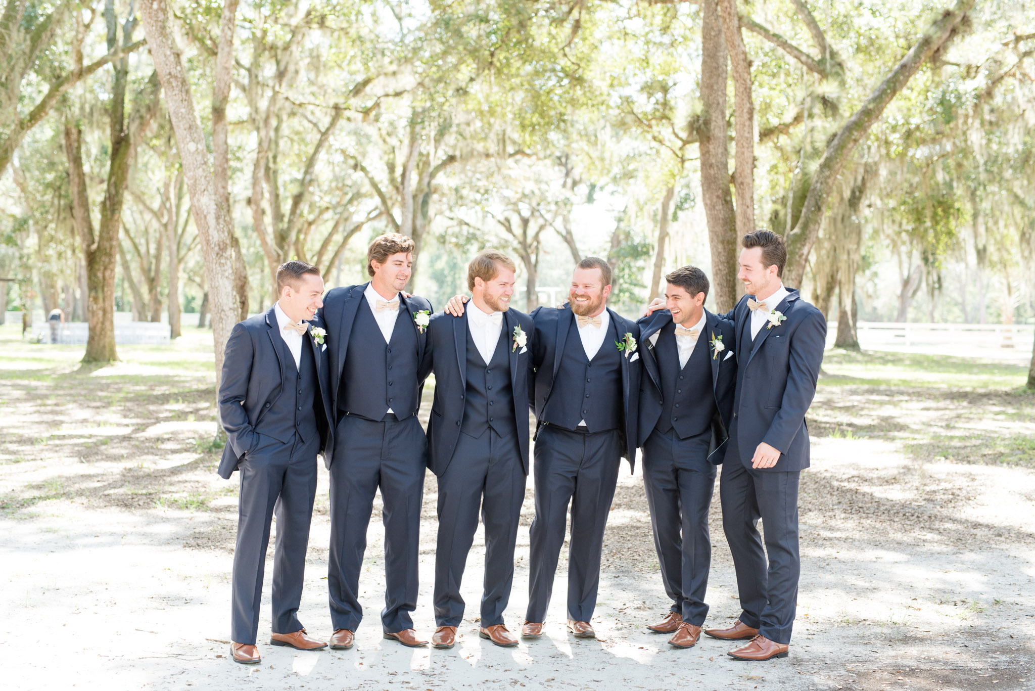 Groom and groomsmen laugh on path.