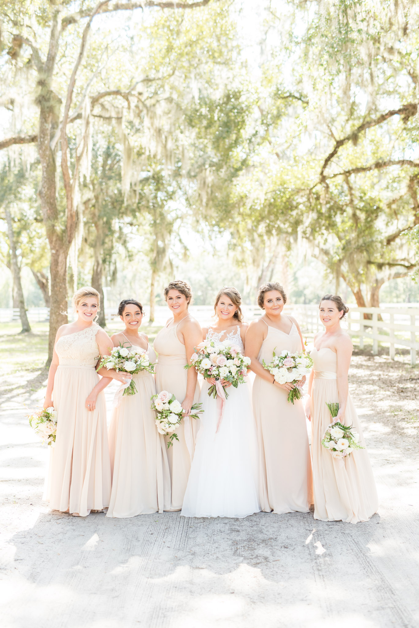 Bridal party smiles at camera with oaks in background.