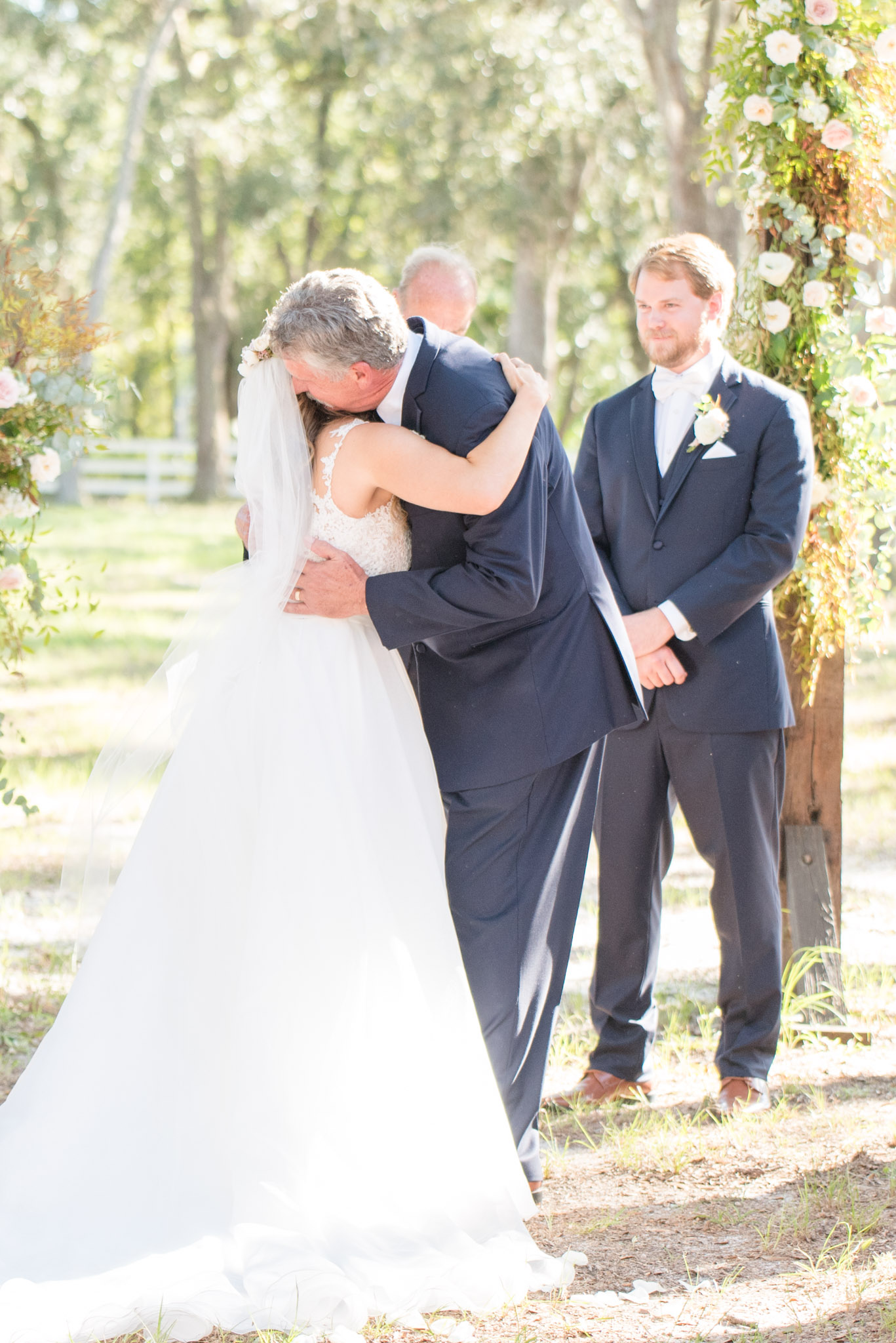 Bride and father hug during wedding ceremony.