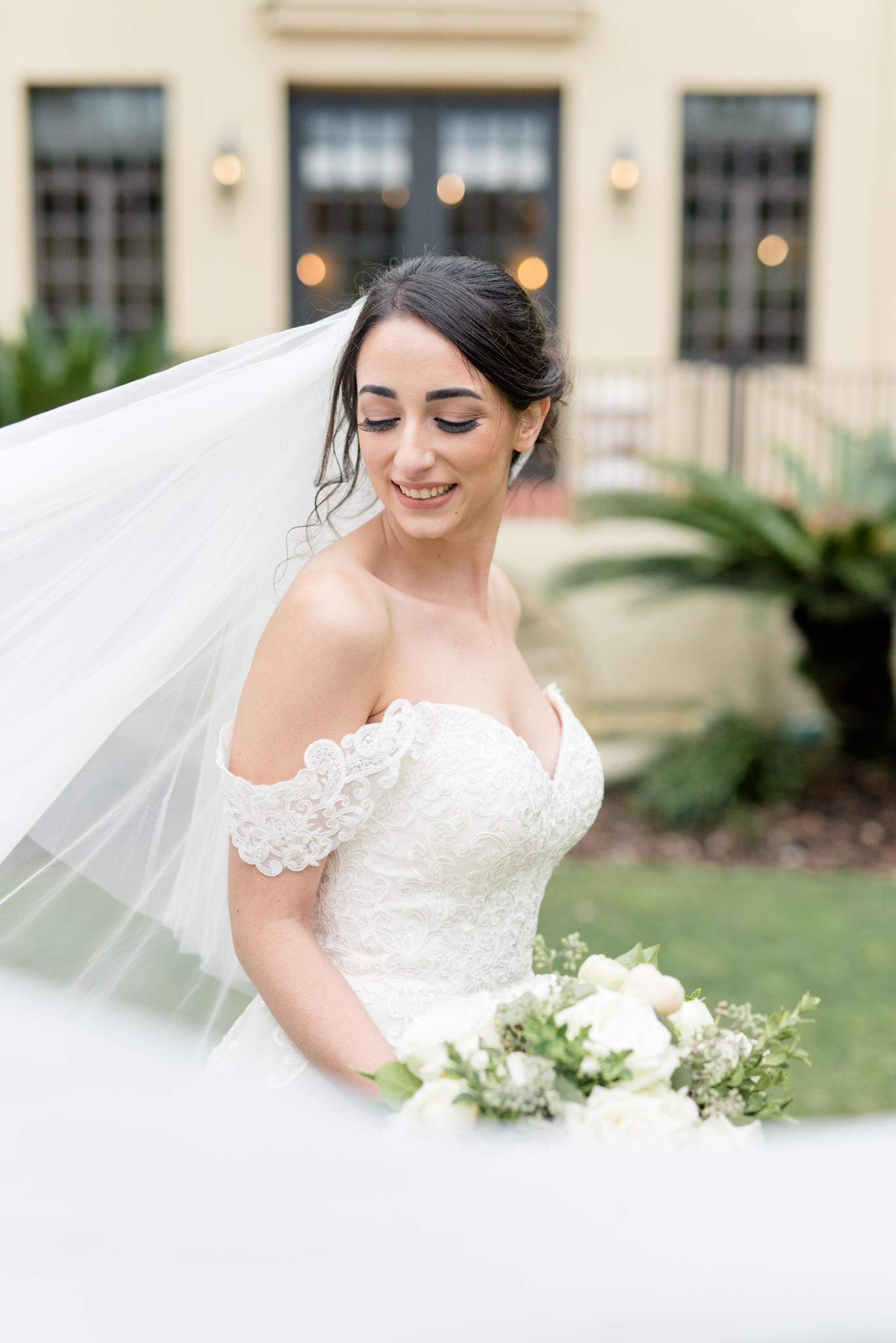 Bride looks over shoulder while veil blows.