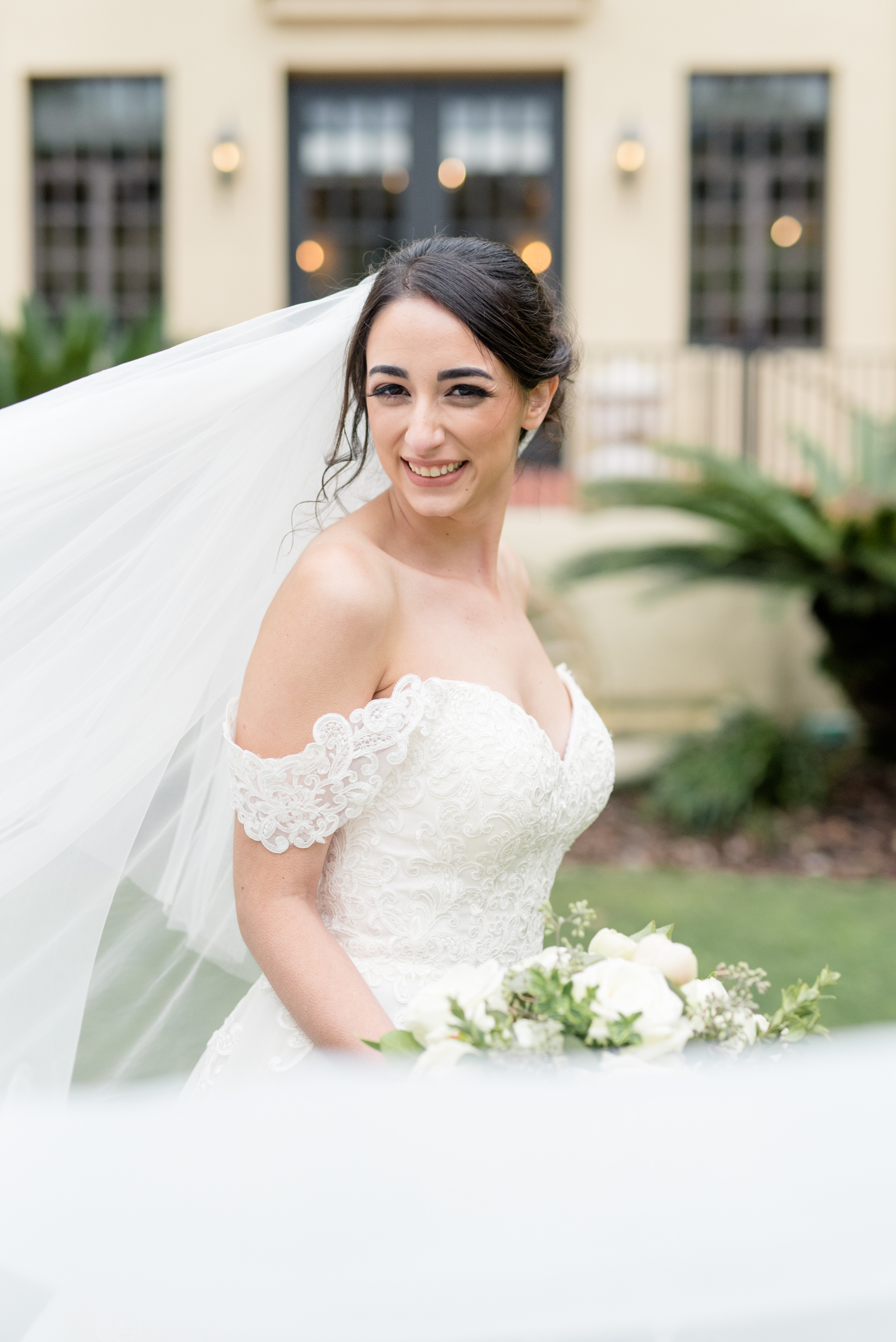Bride smiles at camera as wind blows veil.