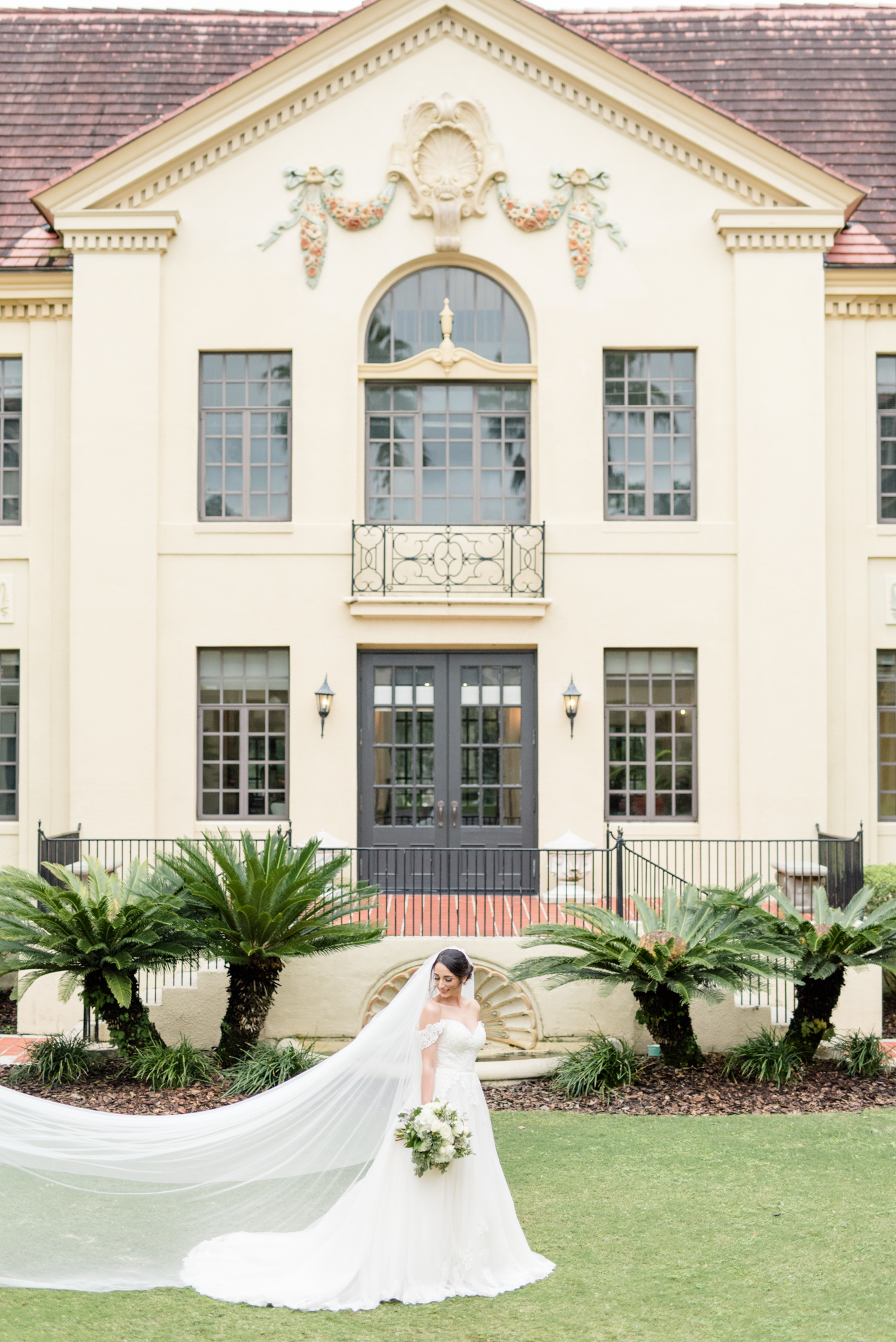 Bride looks over shoulder in front of mansion.