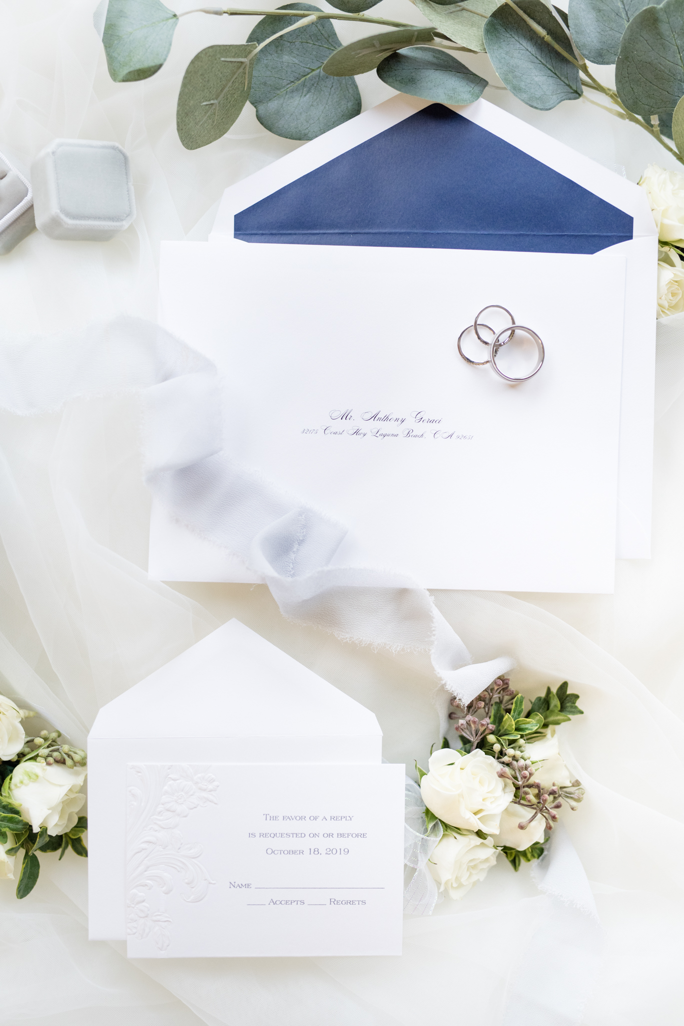 Wedding invitations sits with flowers and rings.
