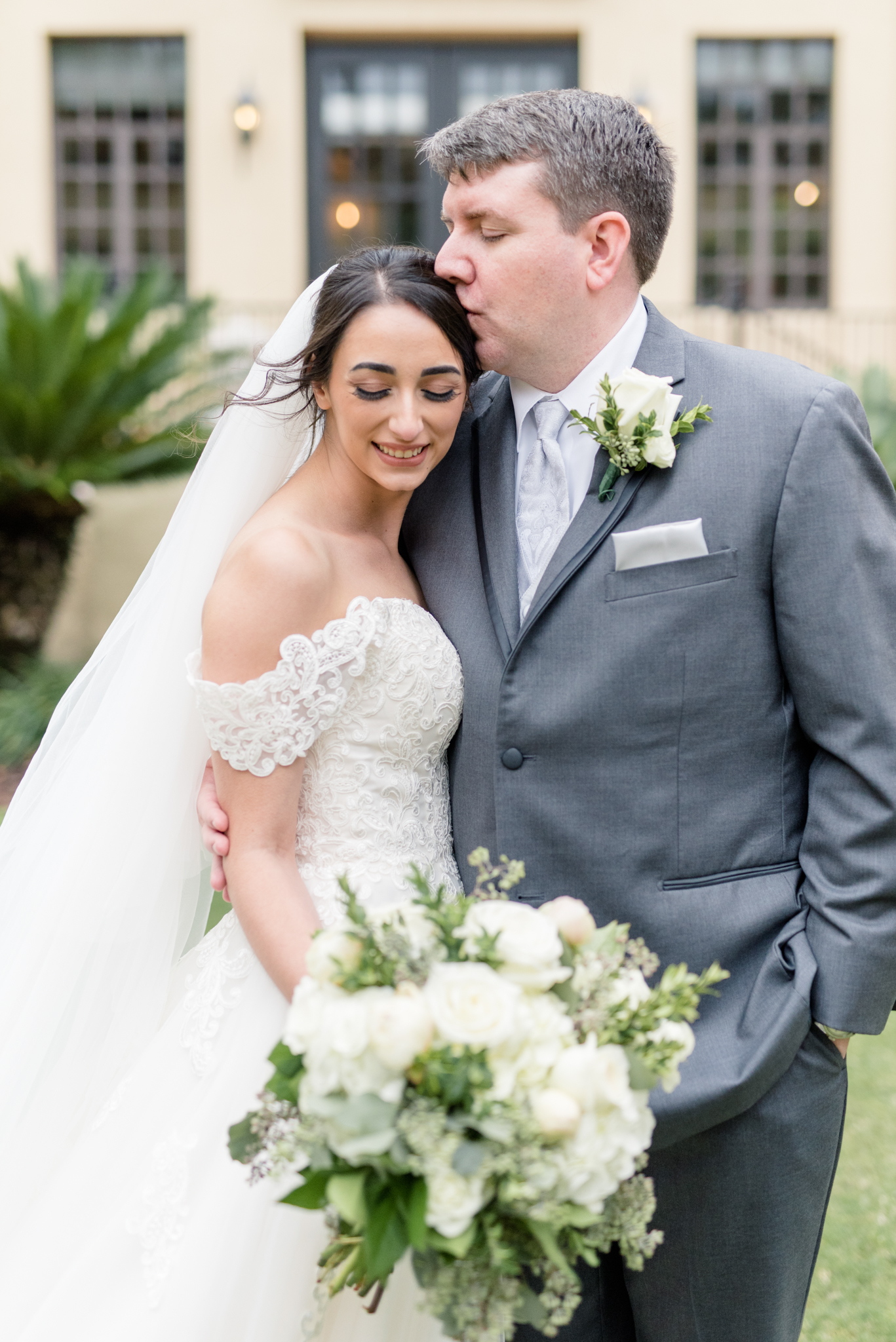 Groom kisses bride on head.