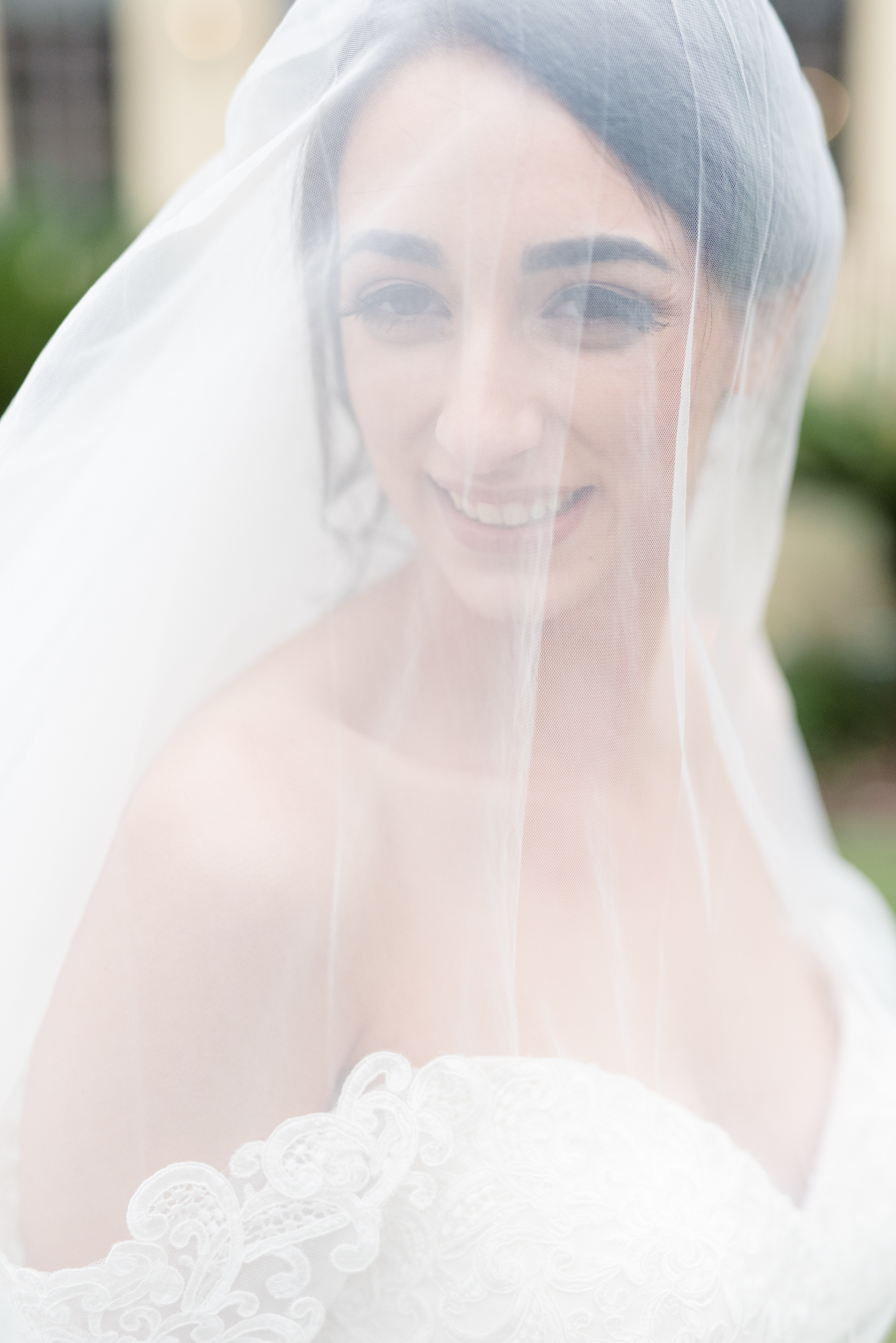 Bride smiles from under veil.