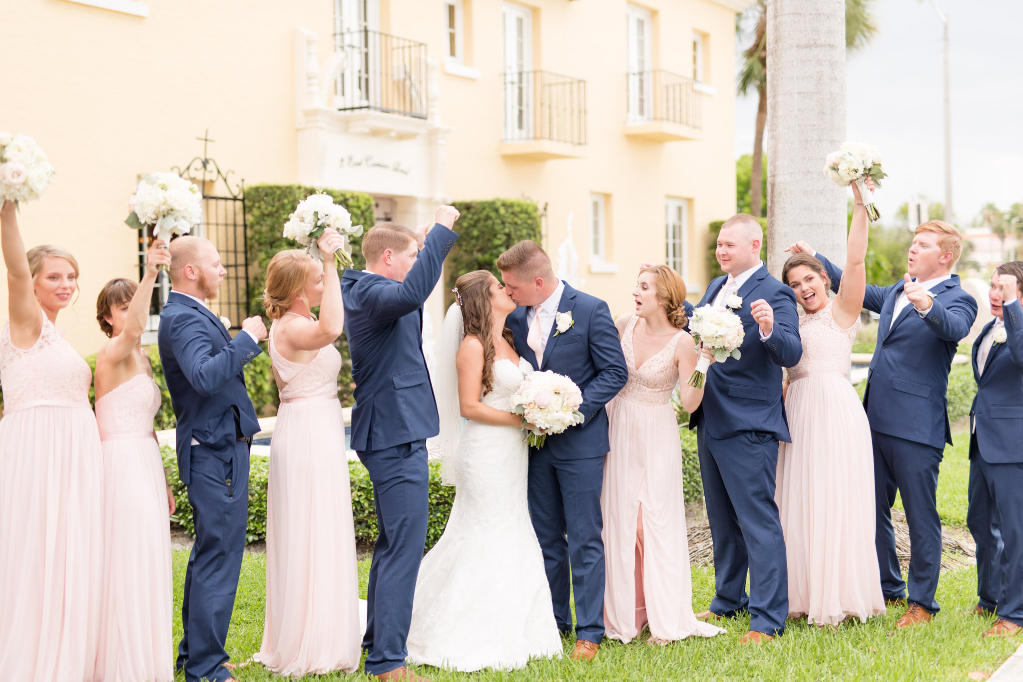 Bride and groom kiss as wedding party cheers together.