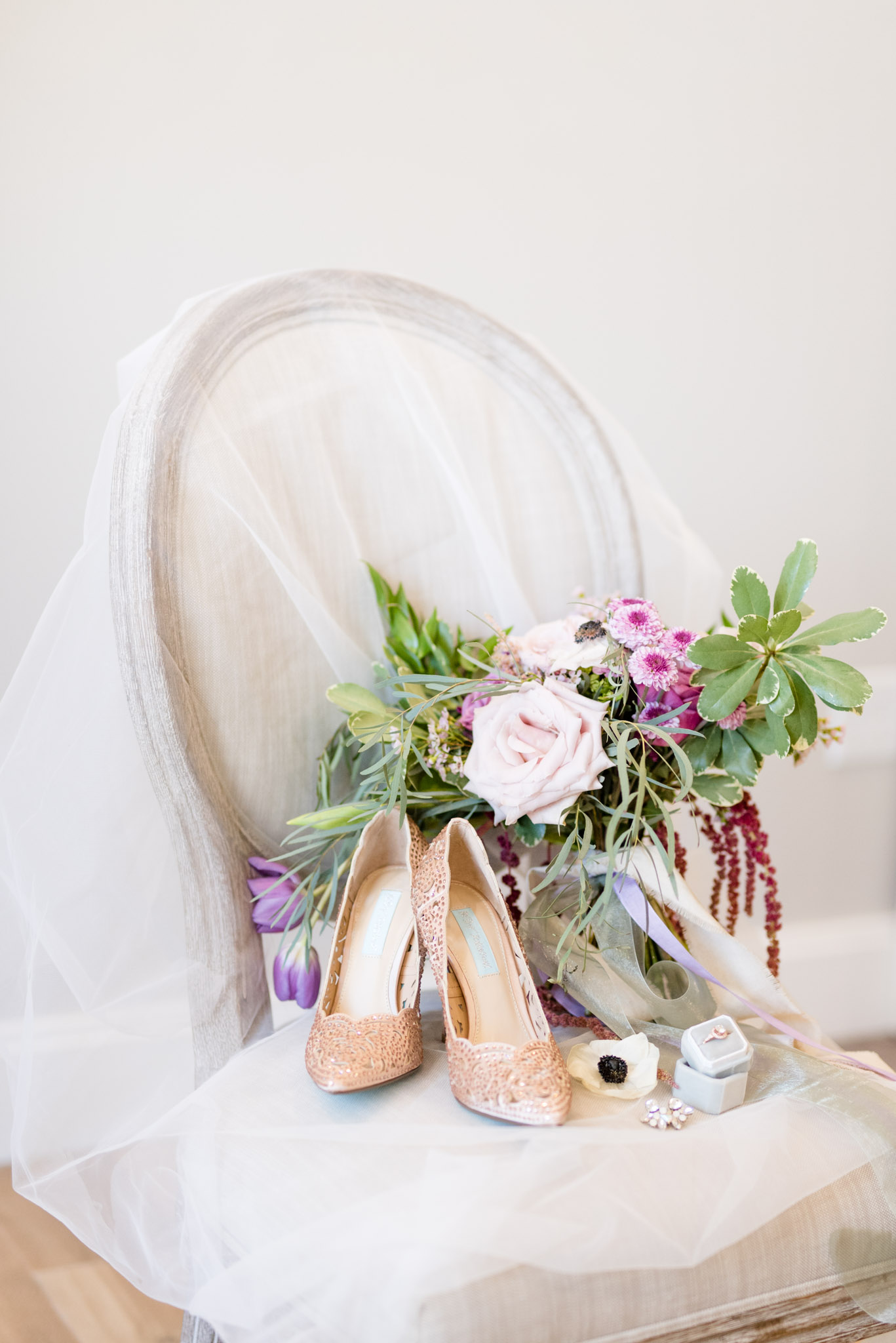 Wedding shoes and bouquet sit on chair.