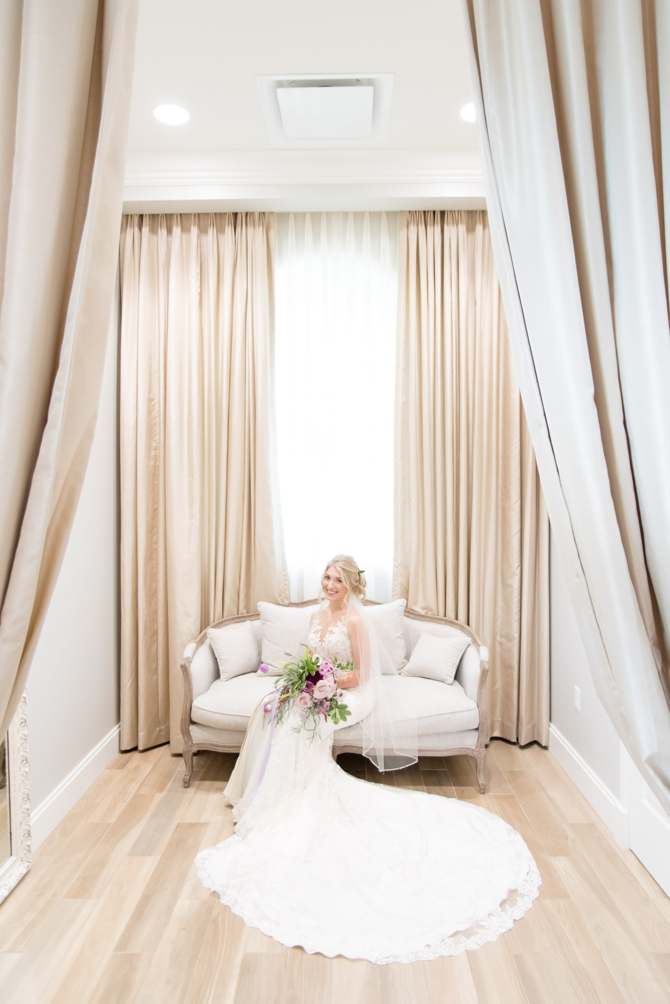Bride sits on couch and smiles at camera.