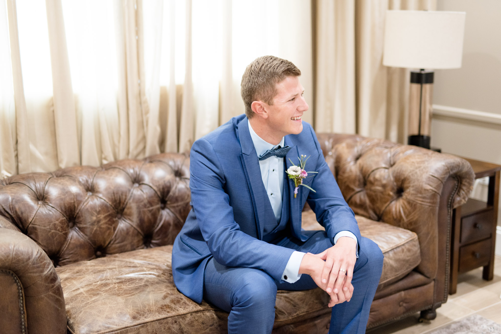 Groom laughs while sitting on couch.