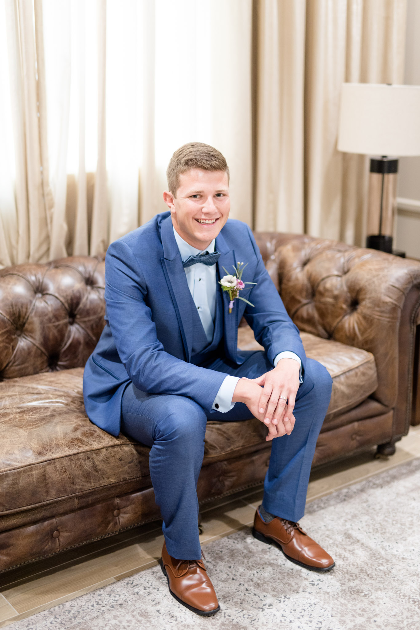 Groom smiles while sits on couch.