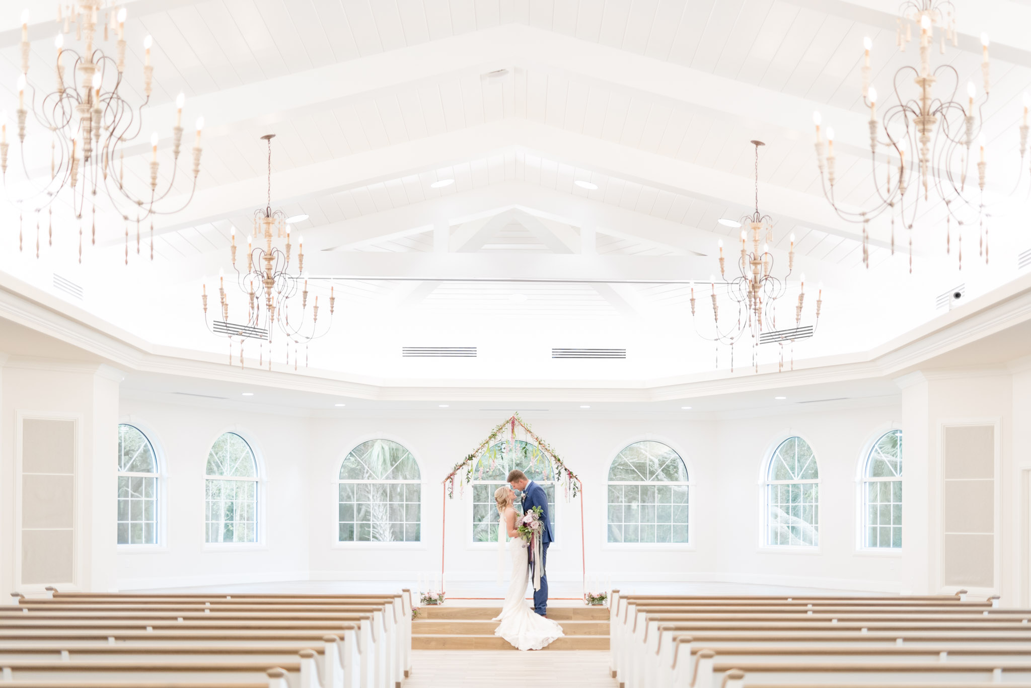 Bride and groom kiss in white chapel.