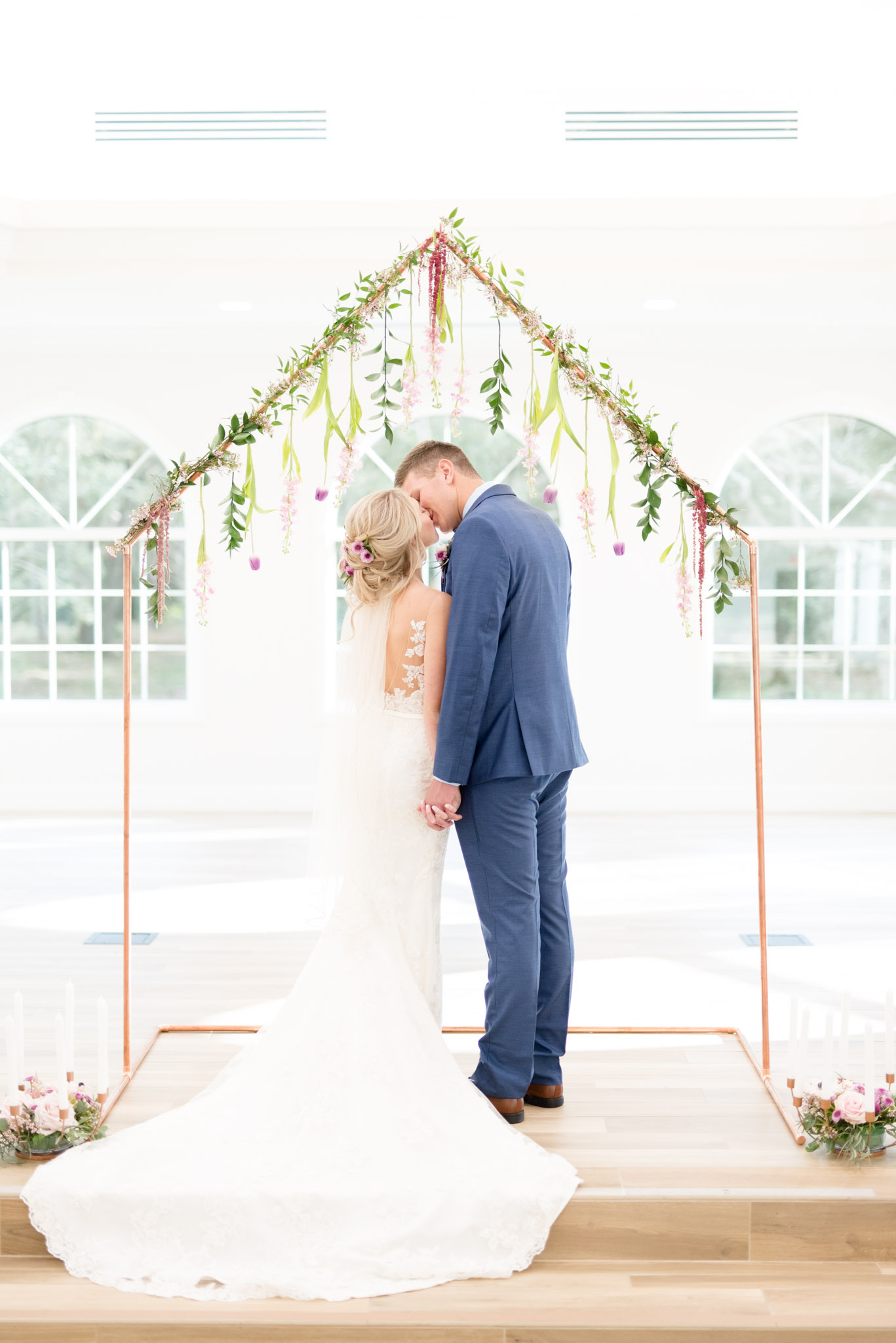 Bride and groom kiss under flower altar.