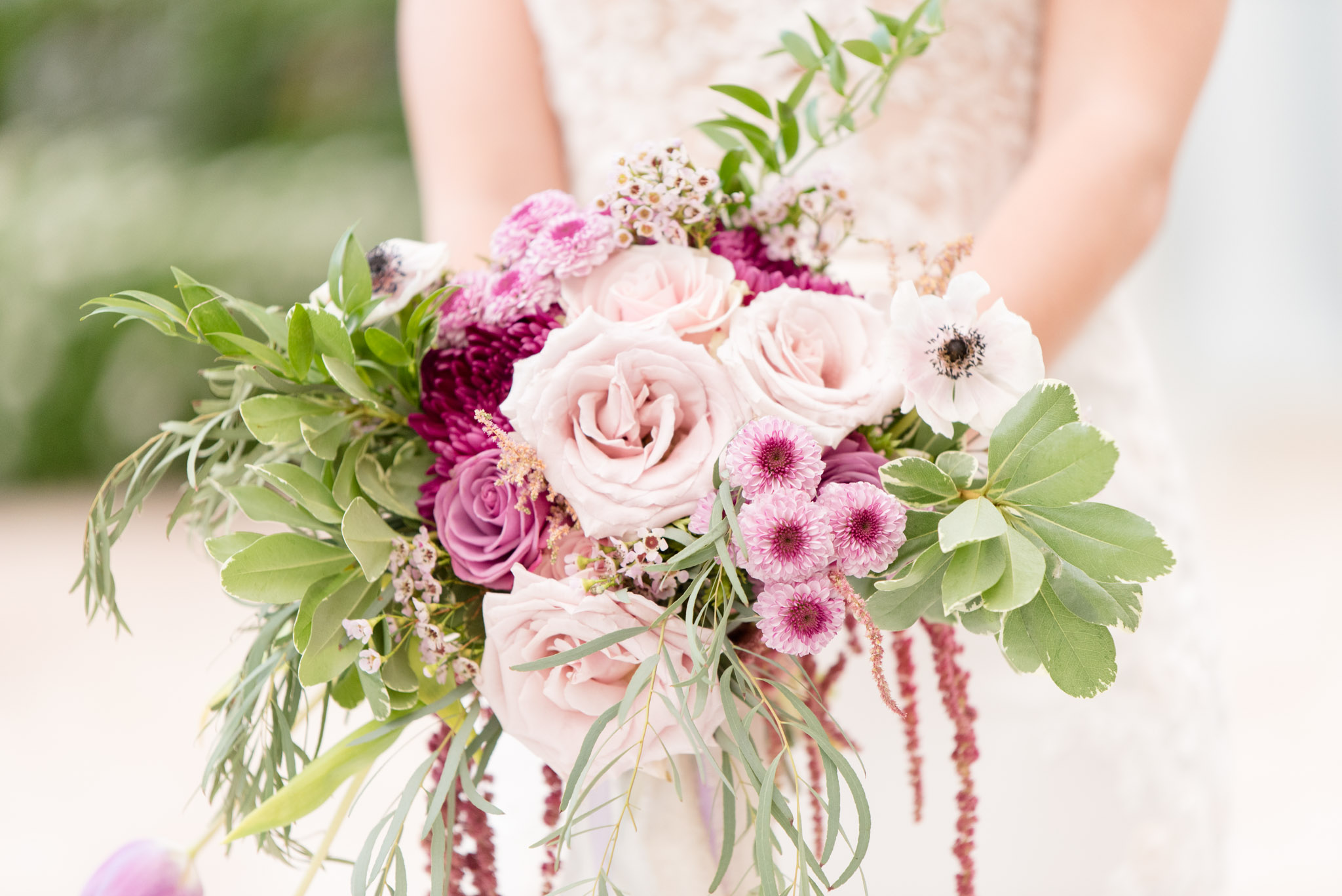 Bride holds bouquet of purple flowers.
