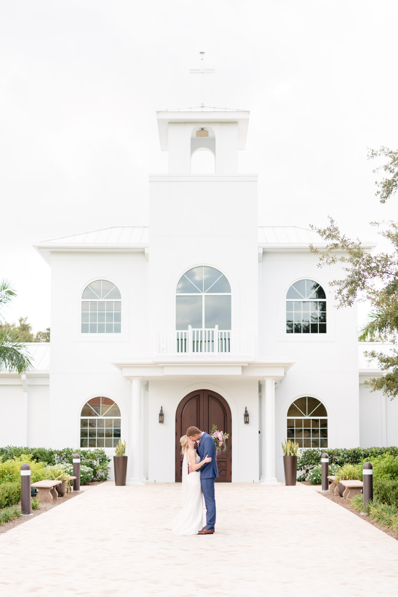 Bride and groom kiss in front of white chapel.