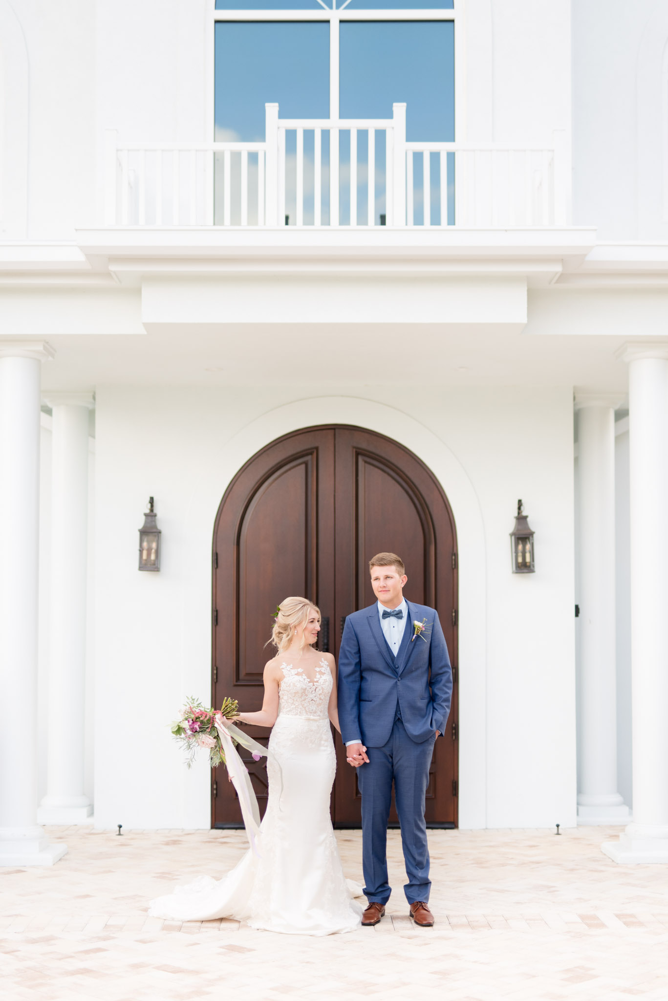 Bride and groom stand in front of chapel doors.