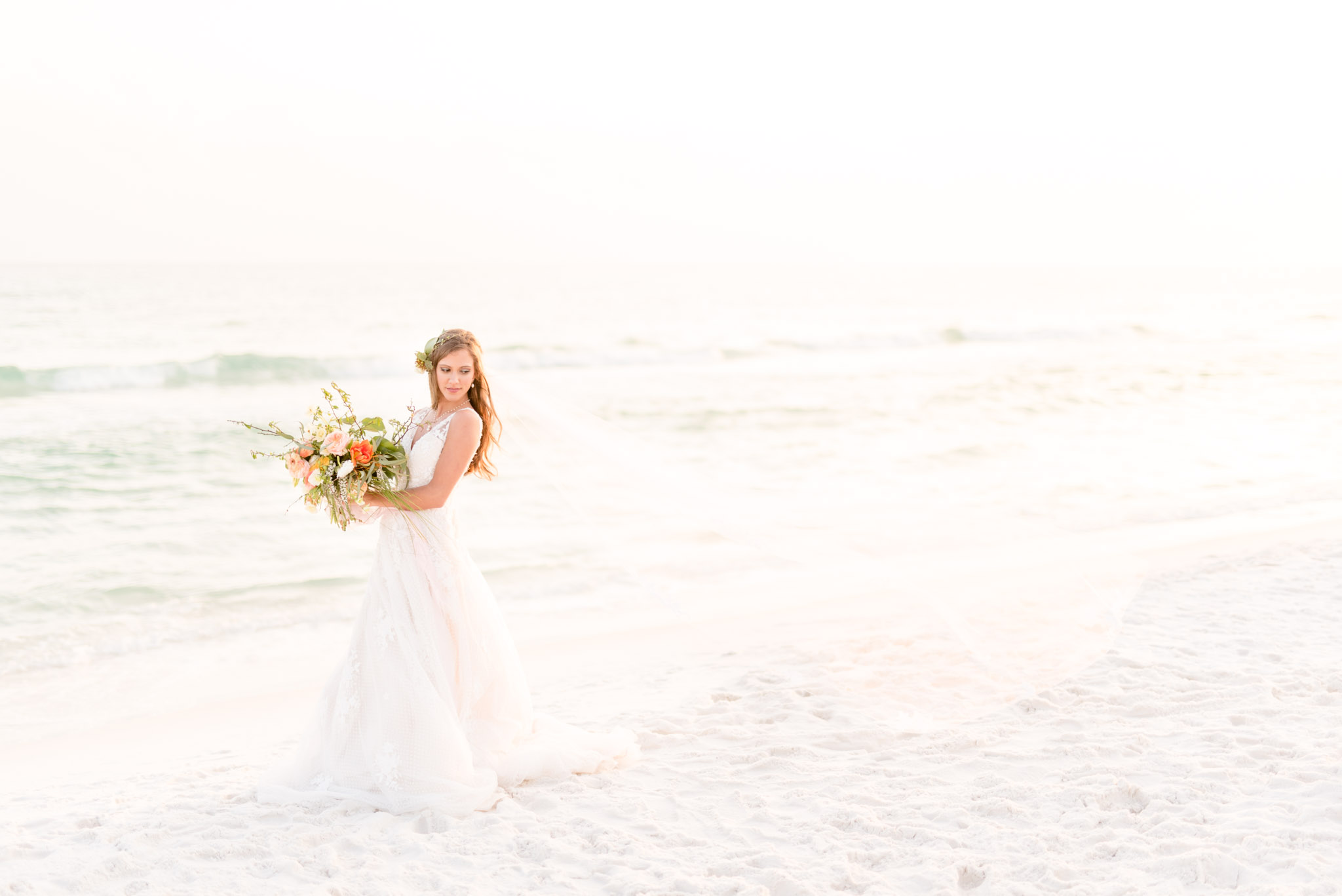 Bride looks over should as veil blows in the ocean breeze.