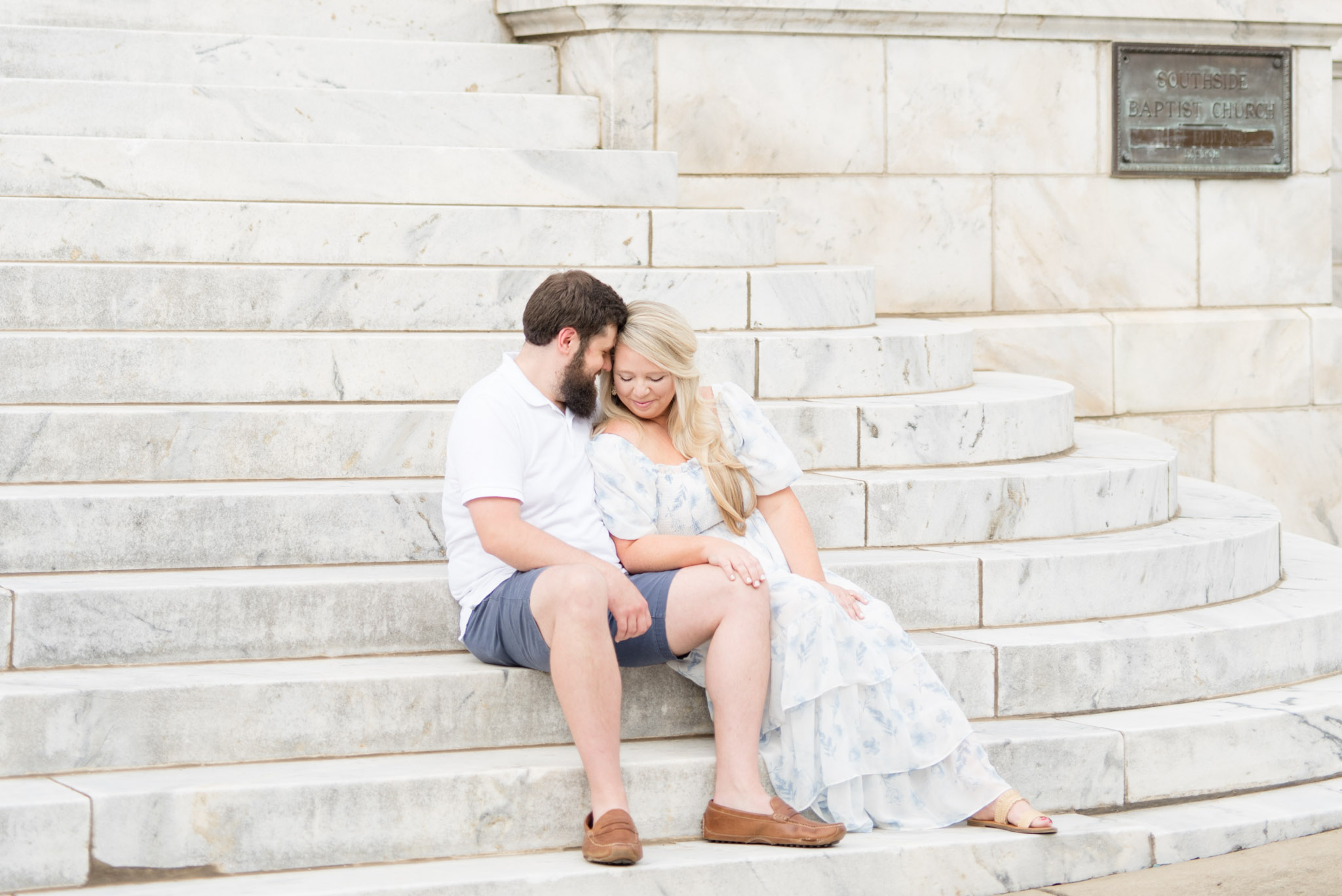 Husband and wife snuggle on marble stairs.