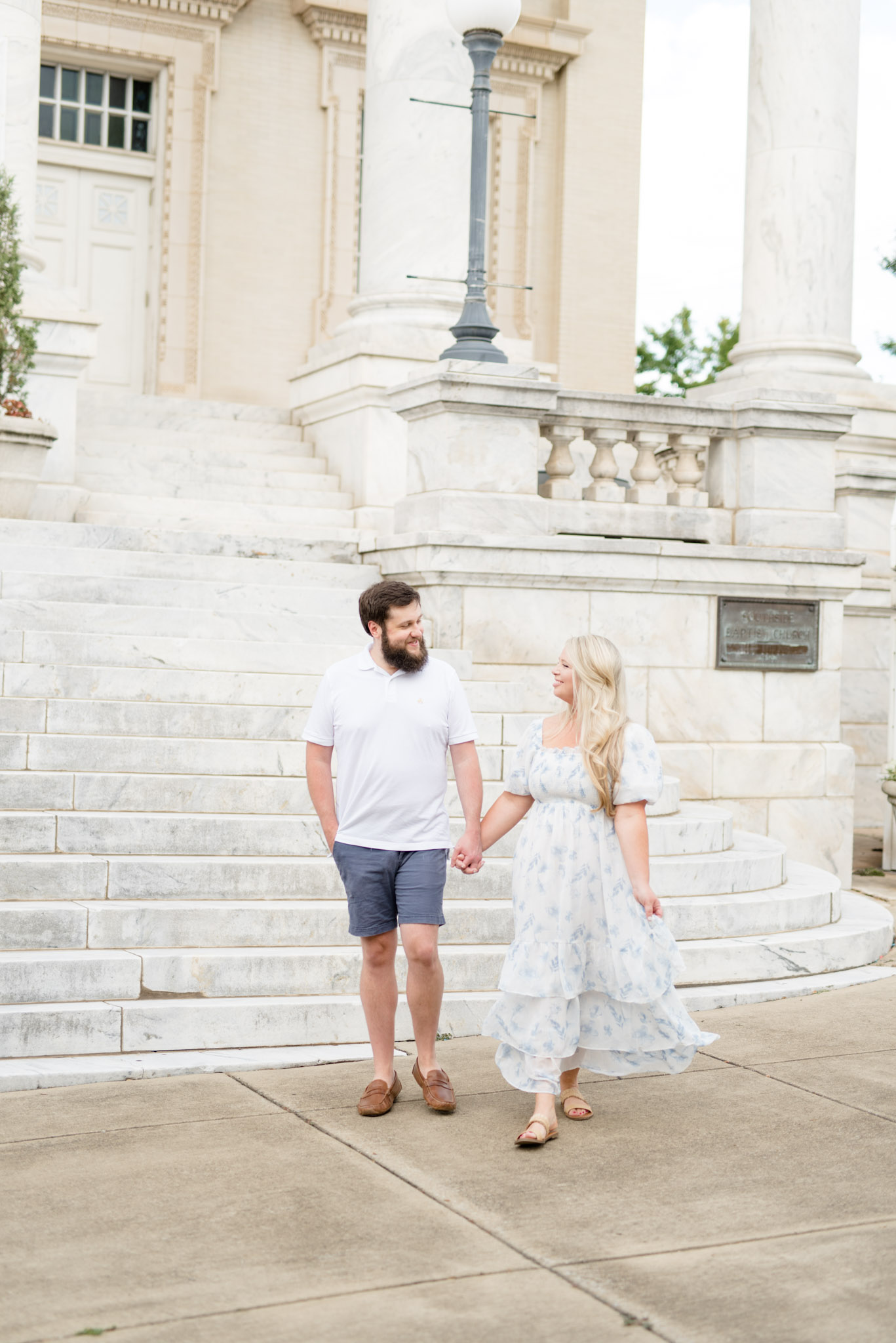 Married couple walks in front of marble stairs.