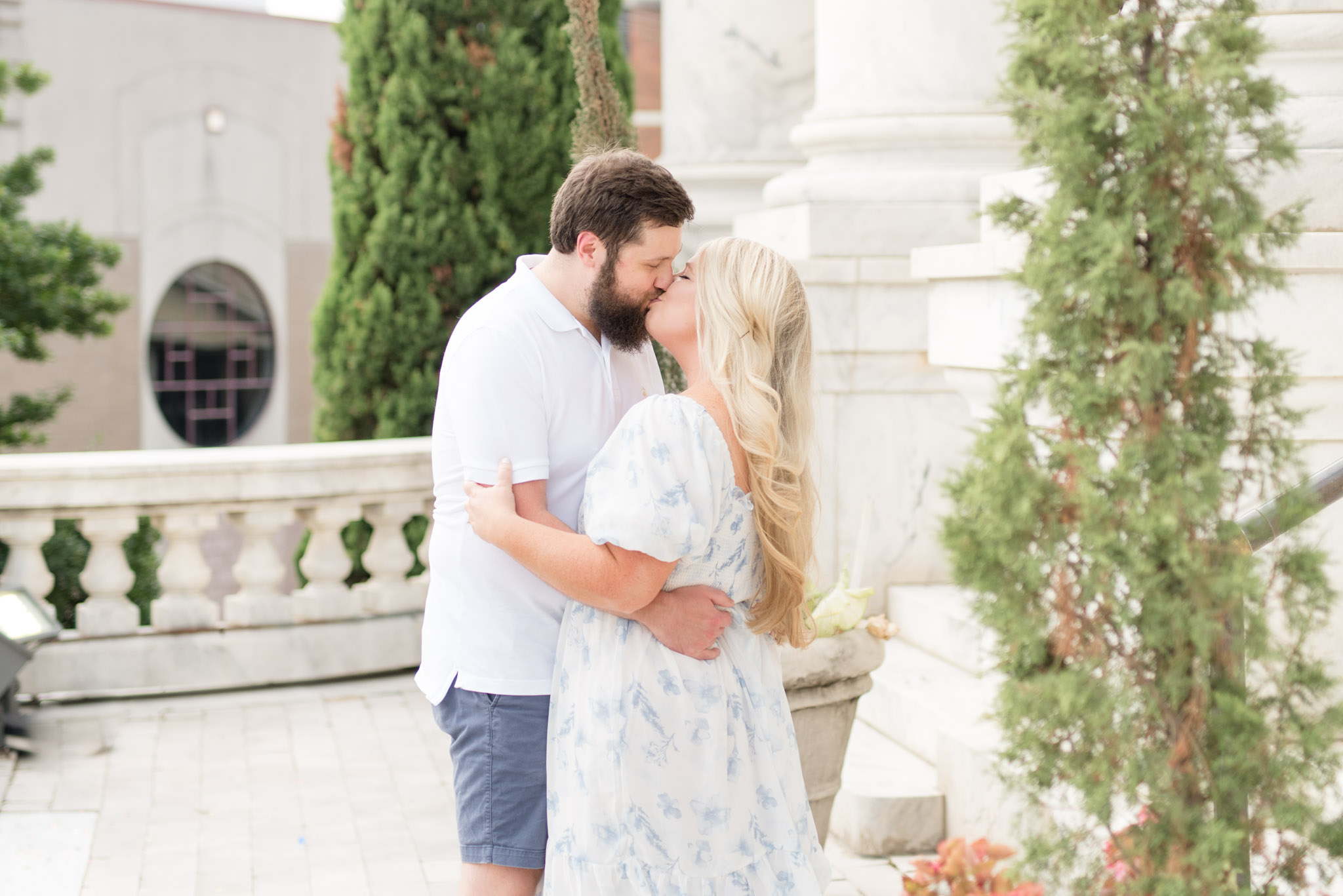 Couple kiss surrounded by white marble columns.